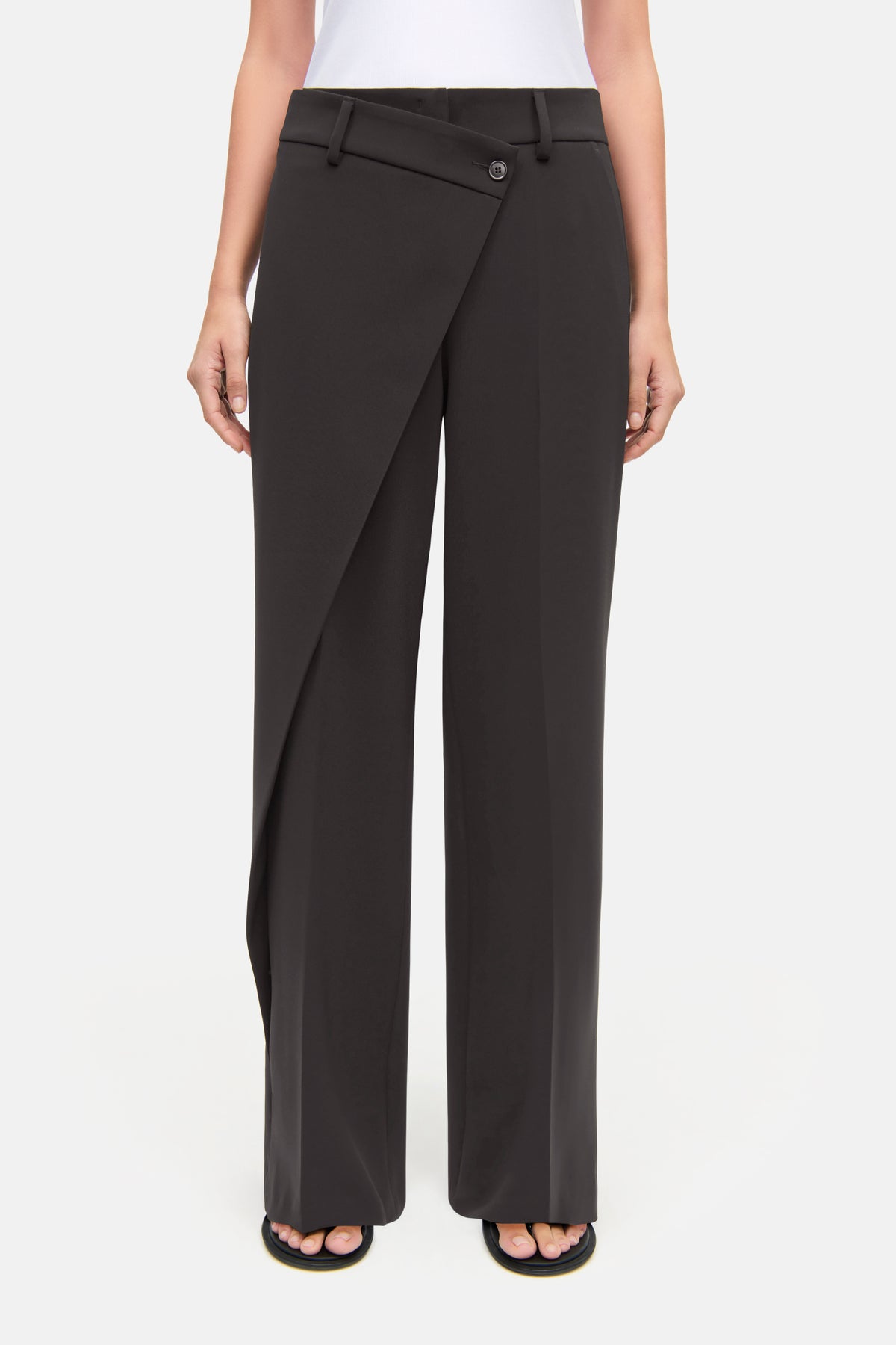 Dunkelbraune Wide-Leg-Hose aus 90 % Polyester und 10 % Polyurethan mit asymmetrischem Wickelbund, getragen in einem Studio.