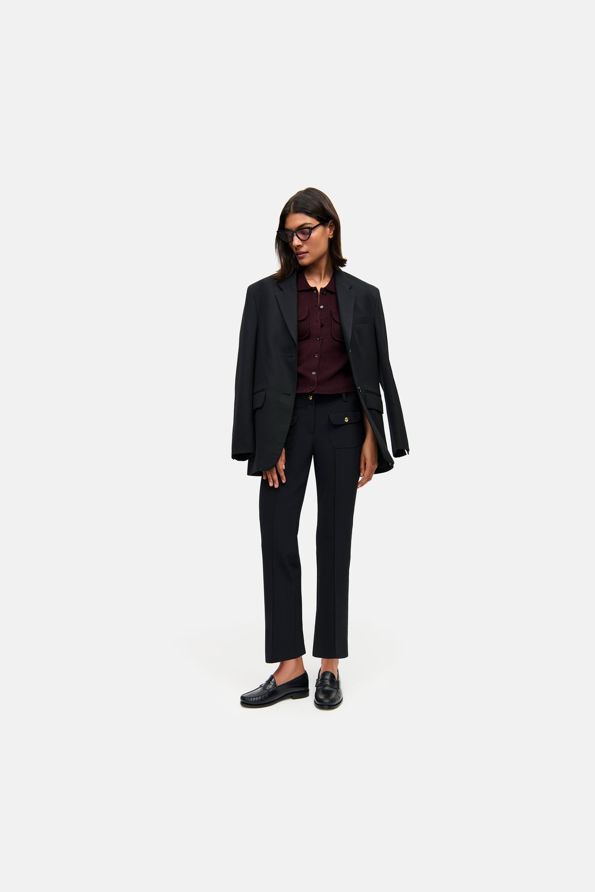 Schwarze, flared Hose aus 88% Polyamid und 12% Elasthan, verkürzte Länge, mit goldenen Knöpfen und aufgesetzten Taschen. Getragen in einem eleganten Business-Setting.