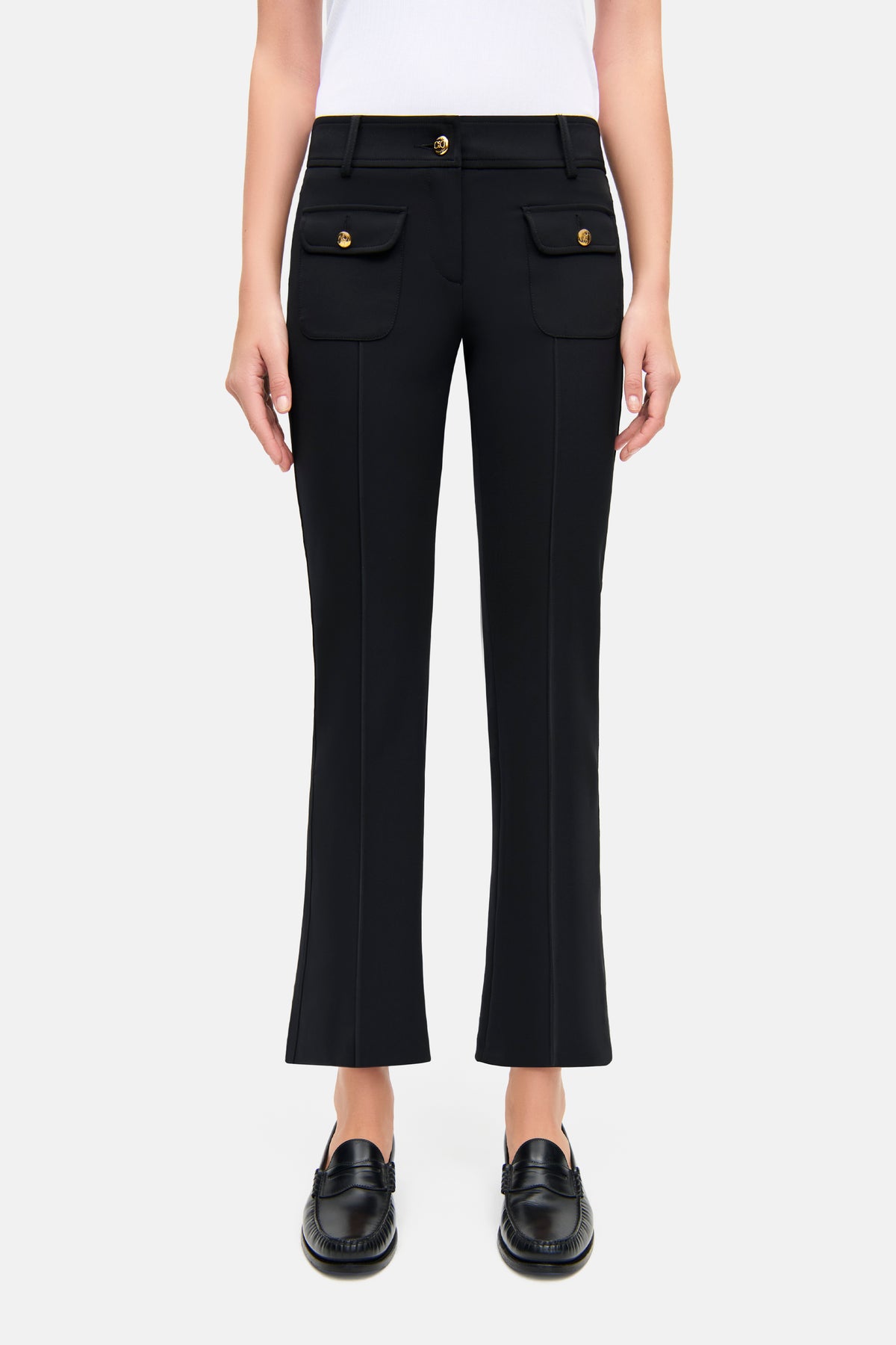 Schwarze Flared-Hose aus Bi-Stretch-Material mit goldenen Knöpfen und aufgenähten Fronttaschen, getragen von einer Person.
