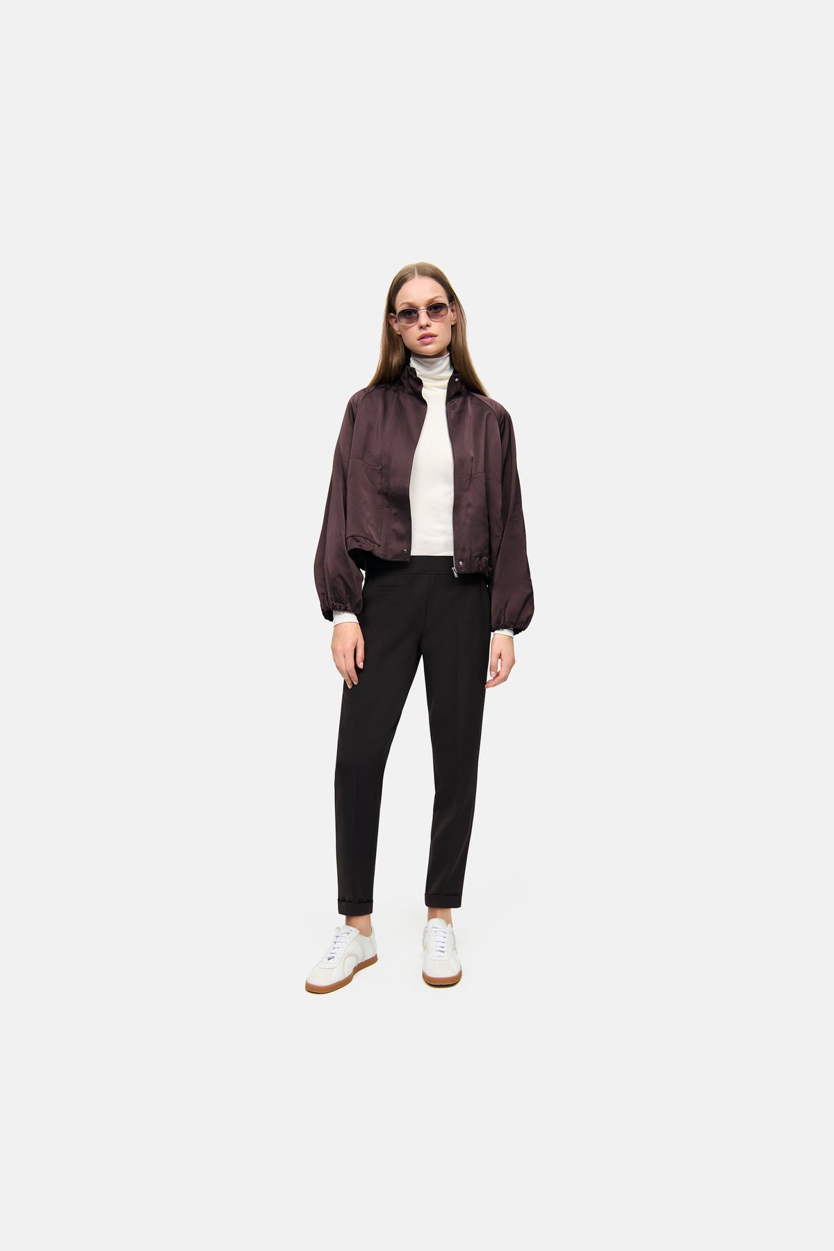 Dunkelbraune Karottenhose aus 63% Polyester, 27% Viskose, 7% Baumwolle, 3% Elasthan. Person in urbanem Setting.