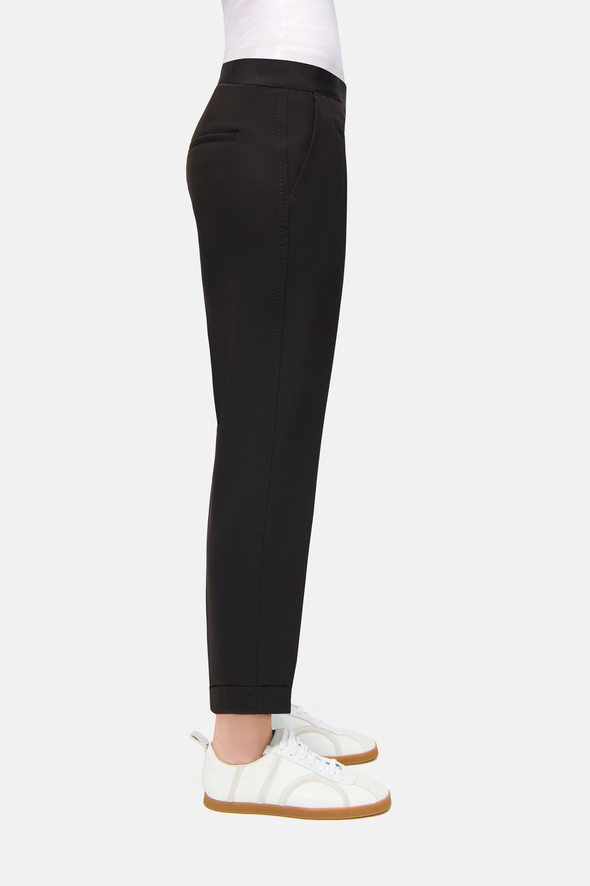 Schwarze Karottenhose aus 63% Polyester, 27% Viskose, 7% Baumwolle, 3% Elasthan, getragen mit weißen Sneakern.
