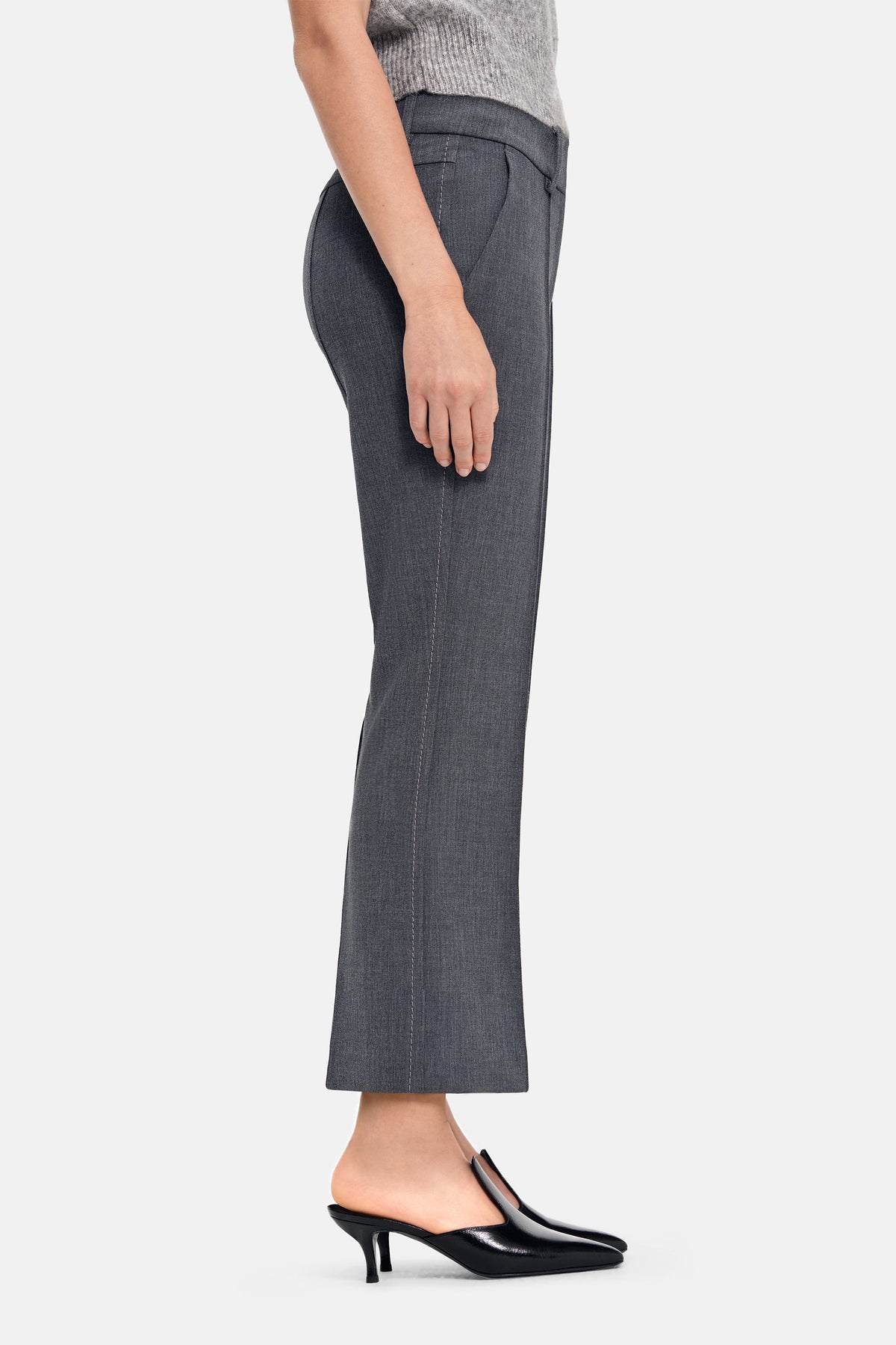 Graue, flared Cropped-Hose aus 63 % Polyester, 27 % Viskose, 7 % Baumwolle und 3 % Elasthan, getragen mit schwarzen Pumps.