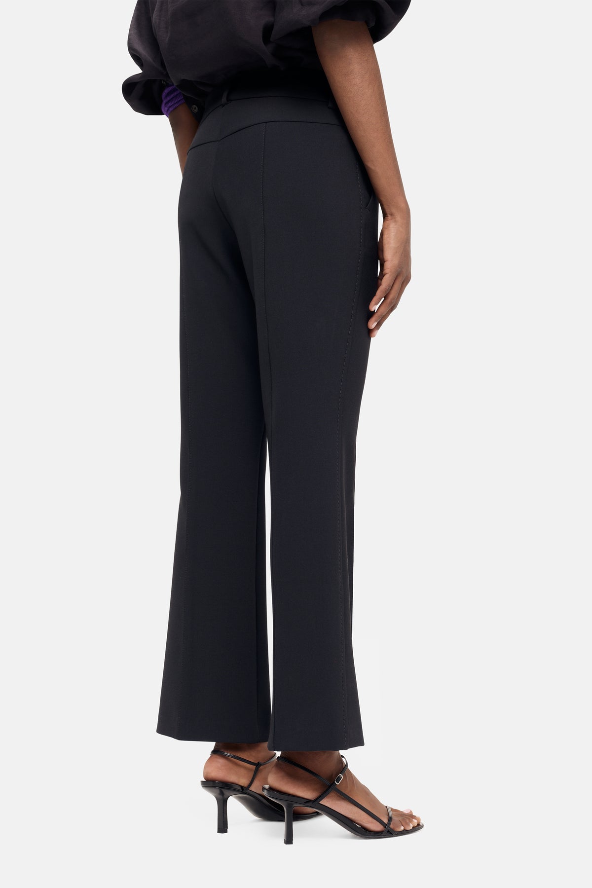 Flared schwarze Hose aus 63% Polyester, 27% Viskose, 7% Baumwolle und 3% Elasthan, getragen mit Absatzsandalen.