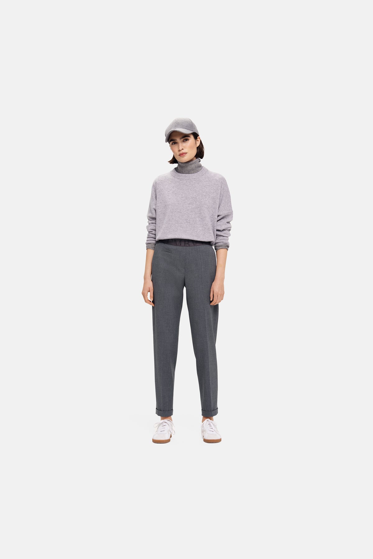 Dunkelgraue Karottenhose aus 67 % Polyester, 29 % Viskose, 4 % Elasthan, getragen in urbanem Setting mit Pullover und Mütze.