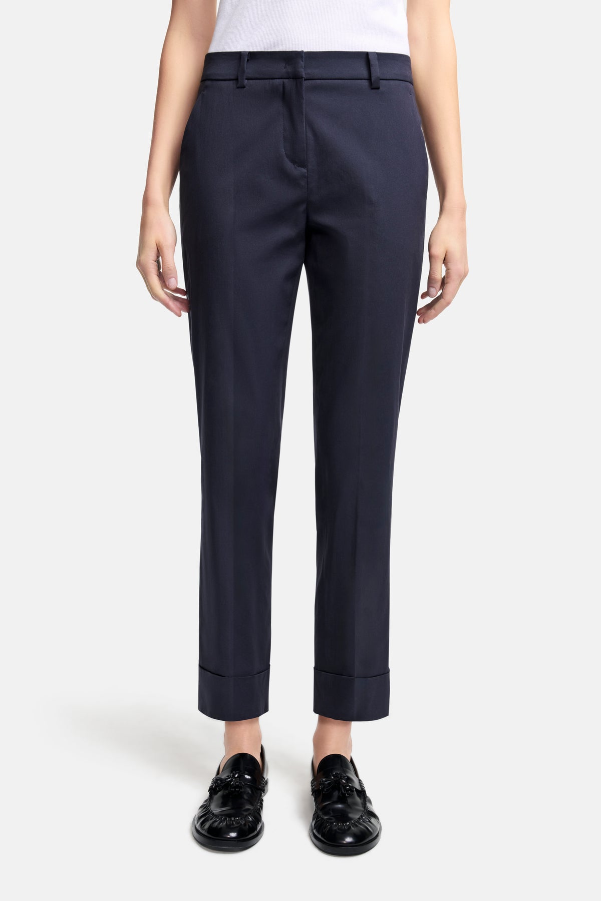 Dunkelblaue Cropped-Hose im Karotten-Schnitt aus 76 % Baumwolle, 21 % Polyamid und 3 % Elasthan. Getragen in einem Studio.