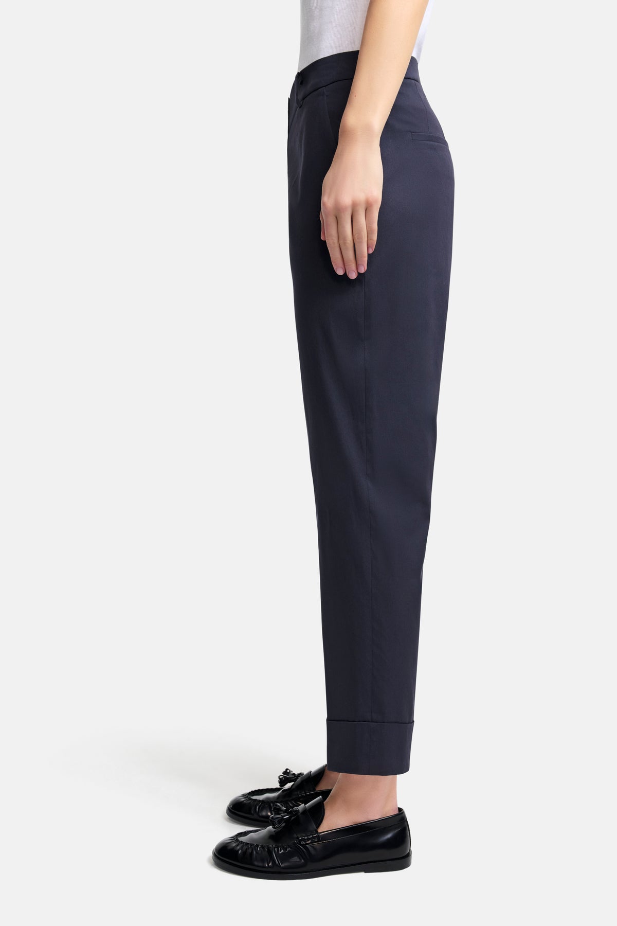 Dunkelblaue Cropped-Hose im Carrot-Fit aus 76% Baumwolle, 21% Polyamid, 3% Elasthan. Getragen mit schwarzen Loafers.