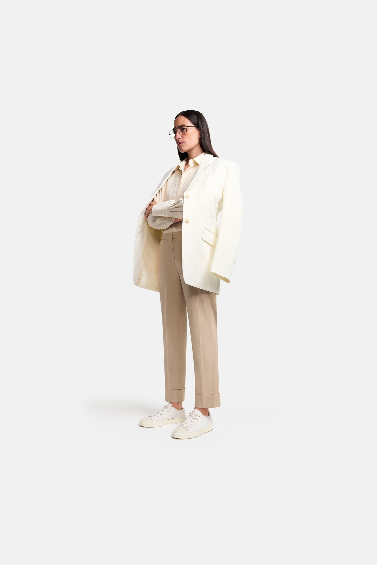 Beige Karottenhose, Baumwollmix, getragen von einer Person in formellem Outfit mit weißem Blazer und Sneakern.