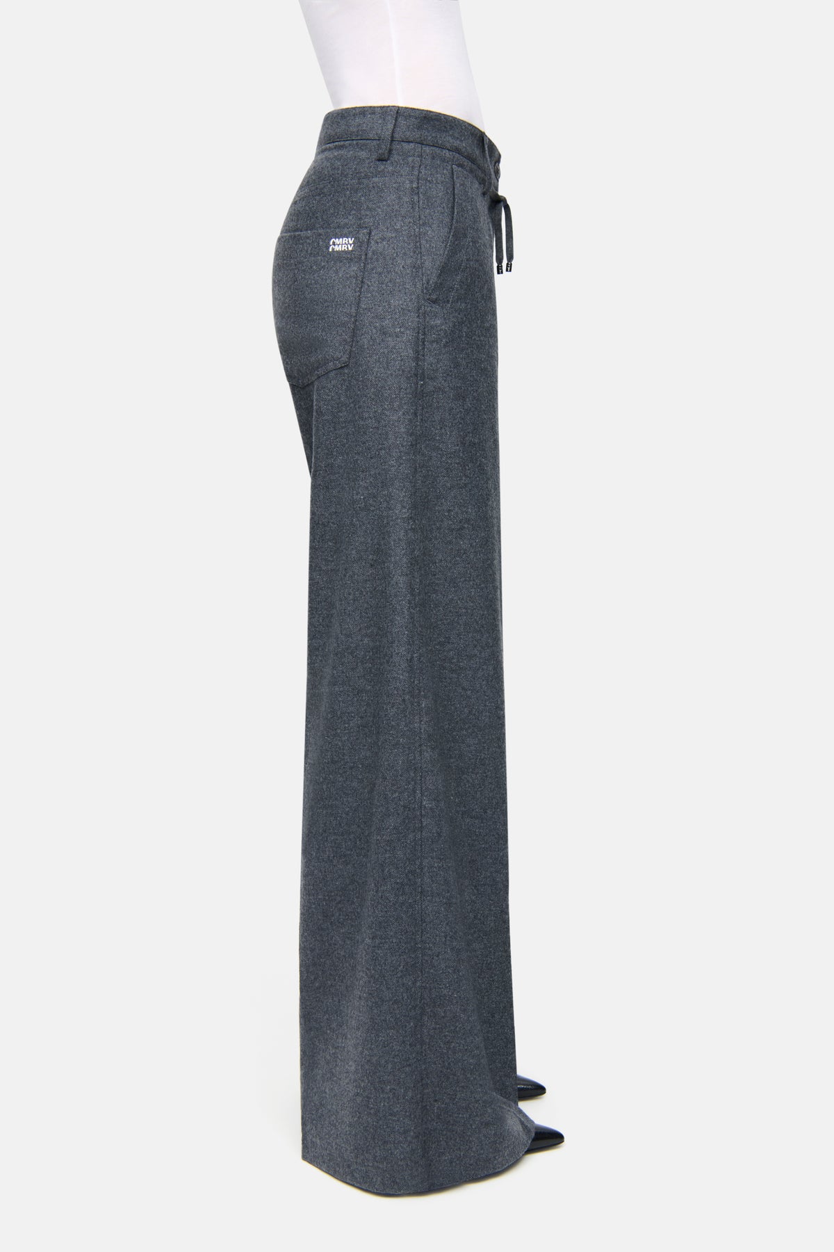 Graue, weit geschnittene Hose aus fließendem Wool Flanell, mit seitlichen Eingrifftaschen und Gesäßtaschen, in einem Indoor-Setting.