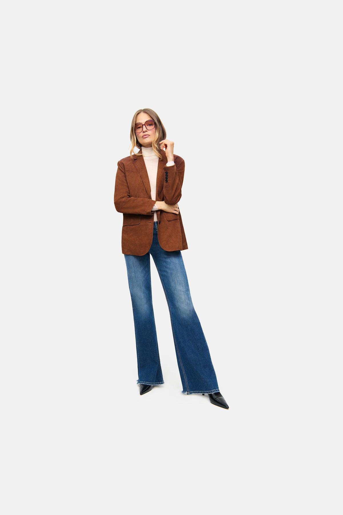 Blauer, flared Baumwoll-Denim mit Destroy-Effekten. Getragen in urbanem Setting mit braunem Blazer und weißem Oberteil.