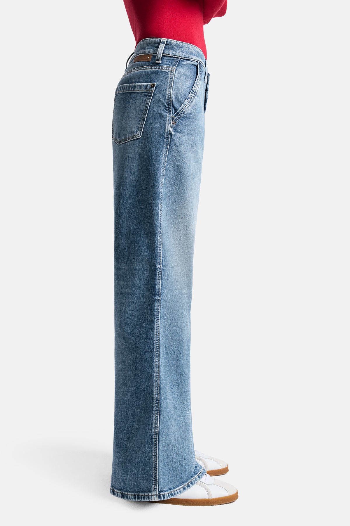 Blaue Wide-Fit Long-Jeans aus 98% Baumwolle und 2% Elasthan. Getragen mit roten Oberteil in Innenraum.