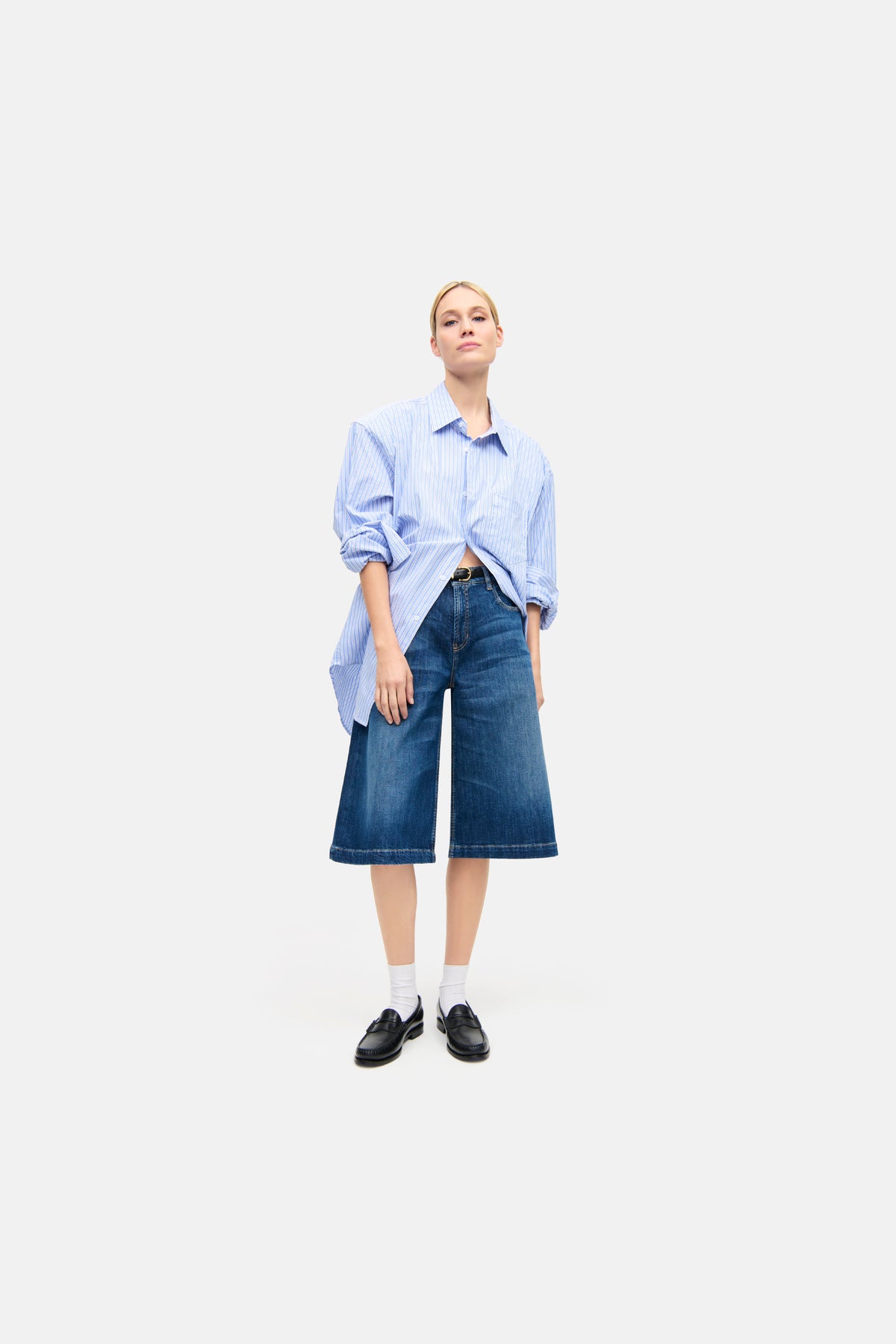 Blaue Palazzo-Bermuda-Shorts aus Denim, 98% Baumwolle, 2% Elasthan. Getragen von einer Person mit Hemd in urbanem Umfeld.
