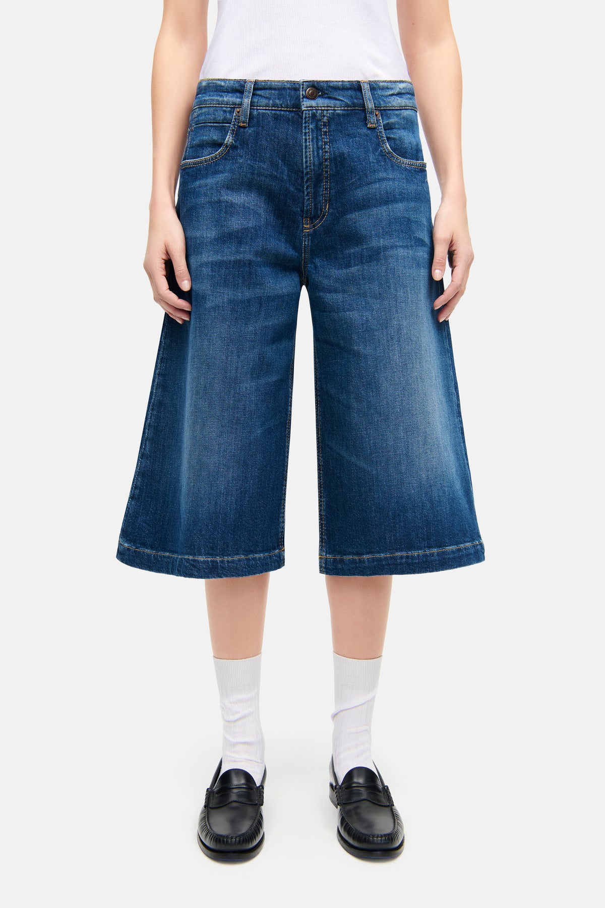 Blaue Palazzo Bermuda-Jeans aus 98 % Baumwolle und 2 % Elasthan, getragen von einer Person. Lässiger Look in urbanem Setting.