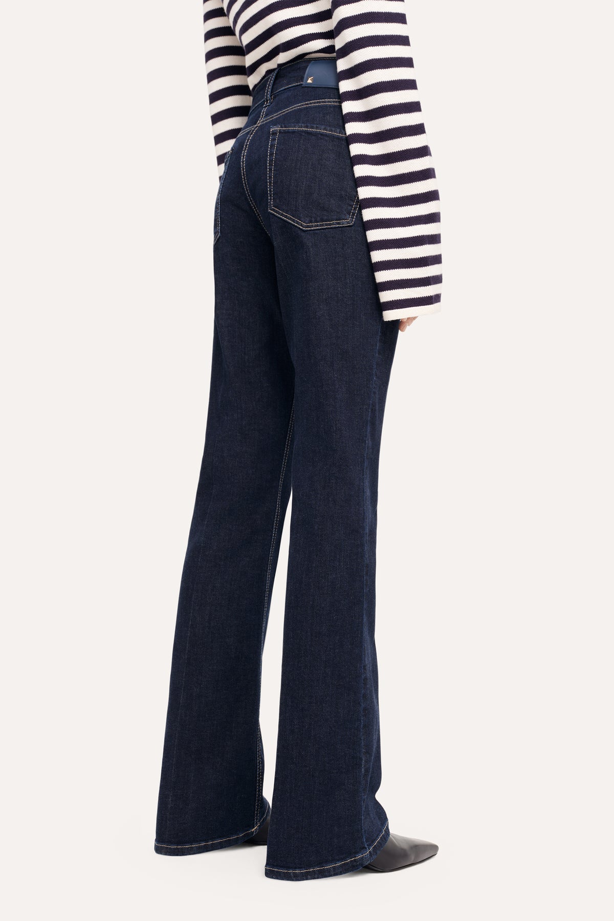 Dunkelblaue Schlaghose aus Denim, getragen von einer Person in einem gestreiften Pullover, Material: 93% Baumwolle, 5% Polyester, 2% Elasthan.