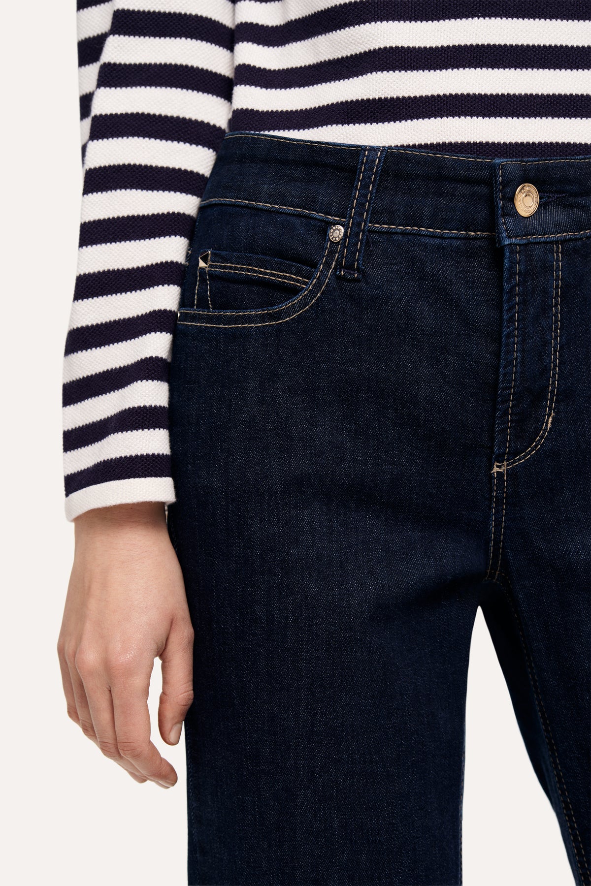 Dunkelblaue, ausgestellte Jeanshose aus 93% Baumwolle, 5% Polyester und 2% Elasthan. Getragen mit gestreiftem Oberteil.