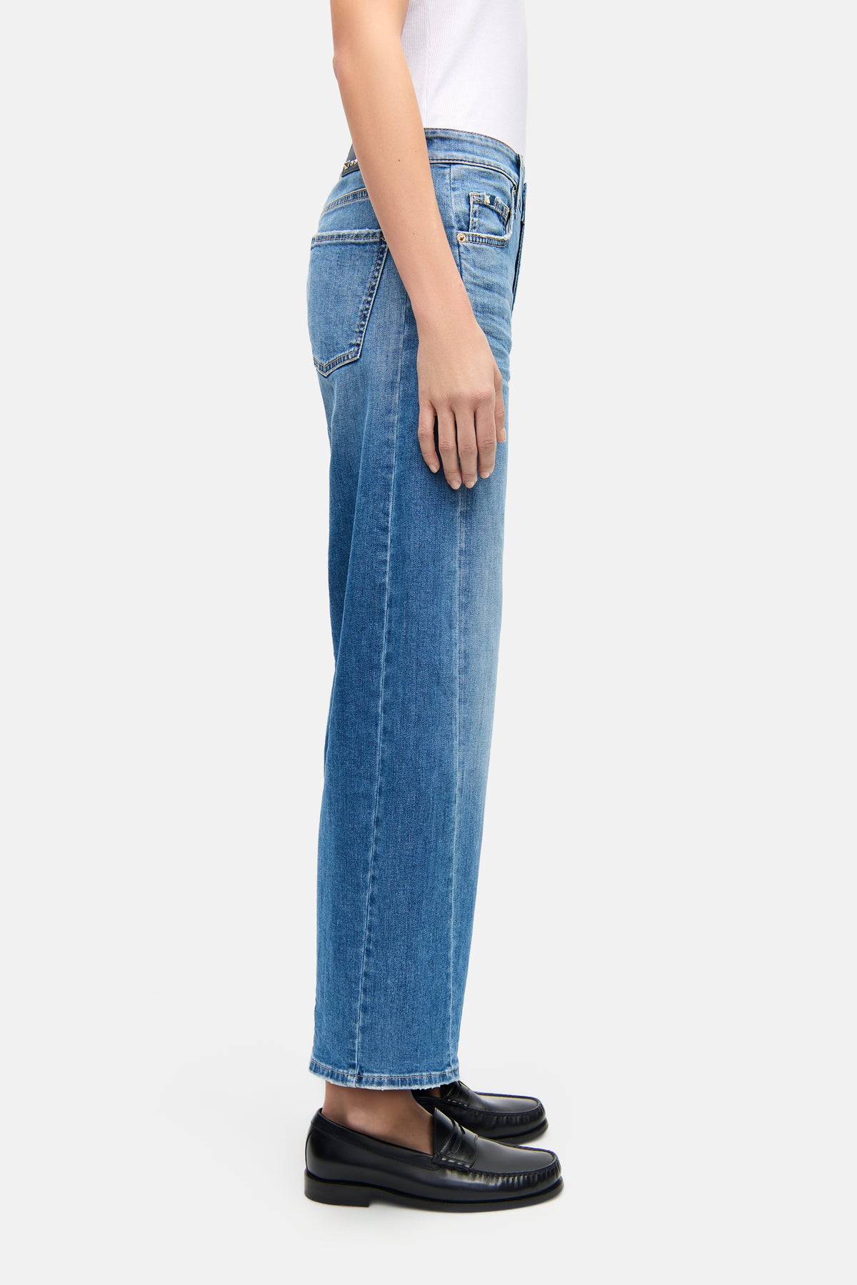 Blaue O-Shape Jeans aus 92% Baumwolle, 6% Elastomultiester T400, 2% Elasthan. Person steht seitlich in einem minimalistischen Setting.
