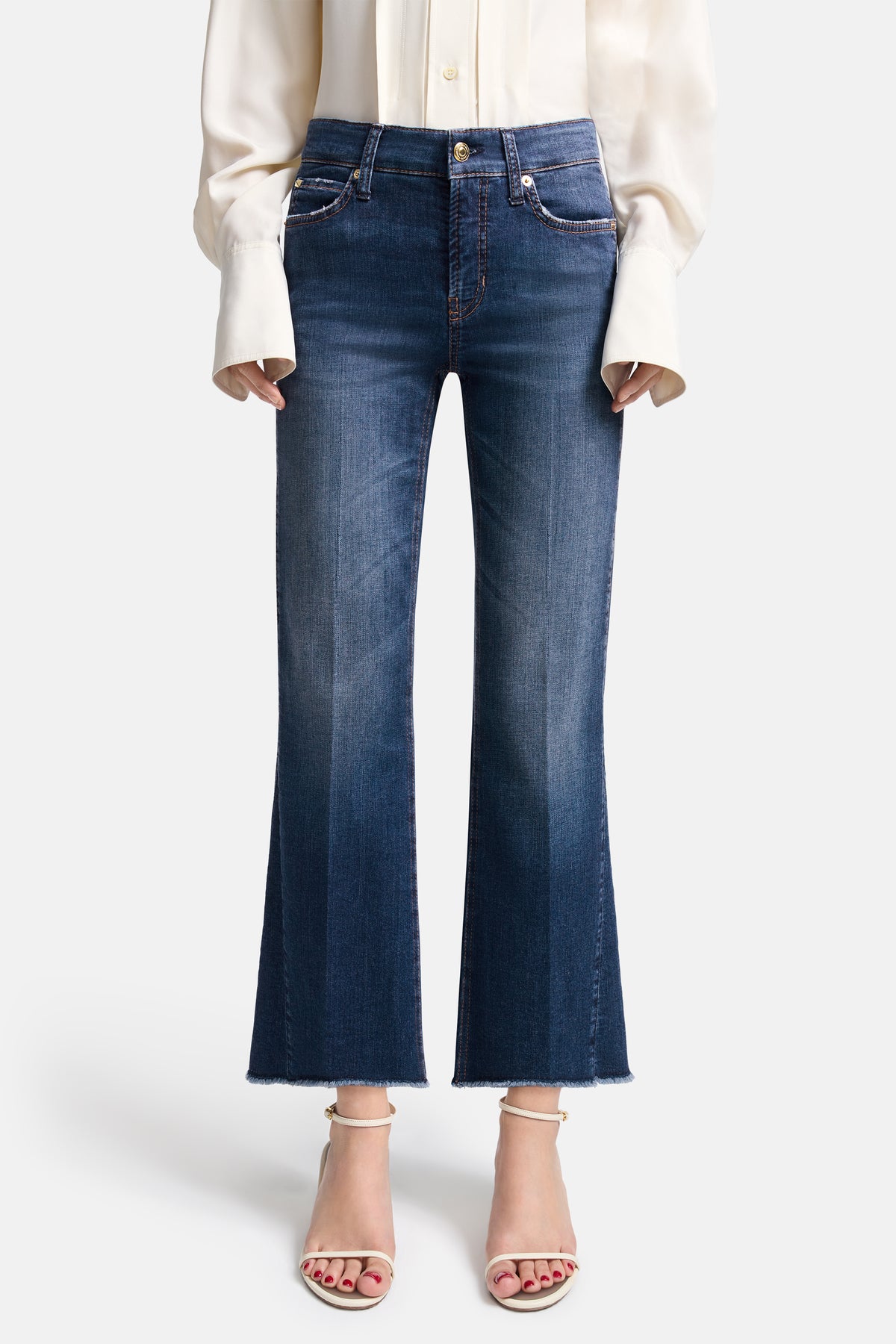 Blaue, verkürzte Flared-Jeans, hergestellt aus 92% Baumwolle, 6% Elastomultiester und 2% Elasthan. Getragen von einer Person in einem Indoor-Setting.