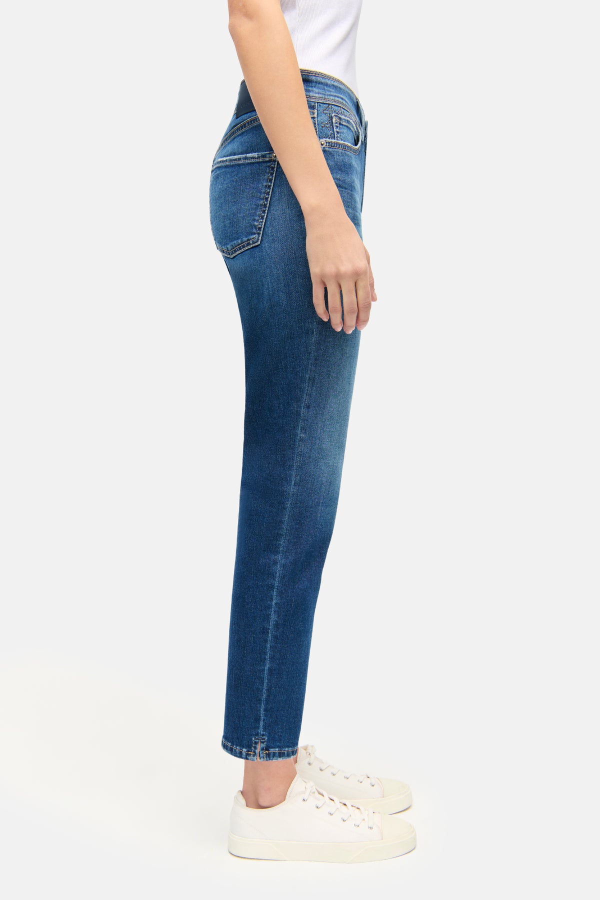 Blaue Slim-Fit-Jeans in verkürzter Länge, 5-Pocket-Stil, aus 92% Baumwolle, 6% Elastomultiester und 2% Elasthan. Getragen mit weißen Sneakers.