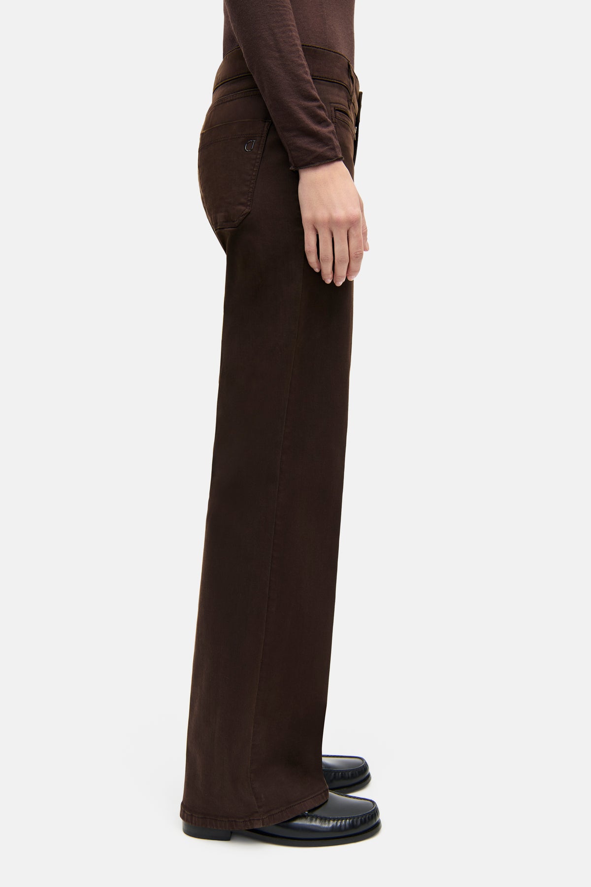 Dunkelbraune weite Jeans aus 94% Baumwolle, 4% Polyester, 2% Elasthan. Seitansicht, getragen von einer Person in einem modernen Setting.