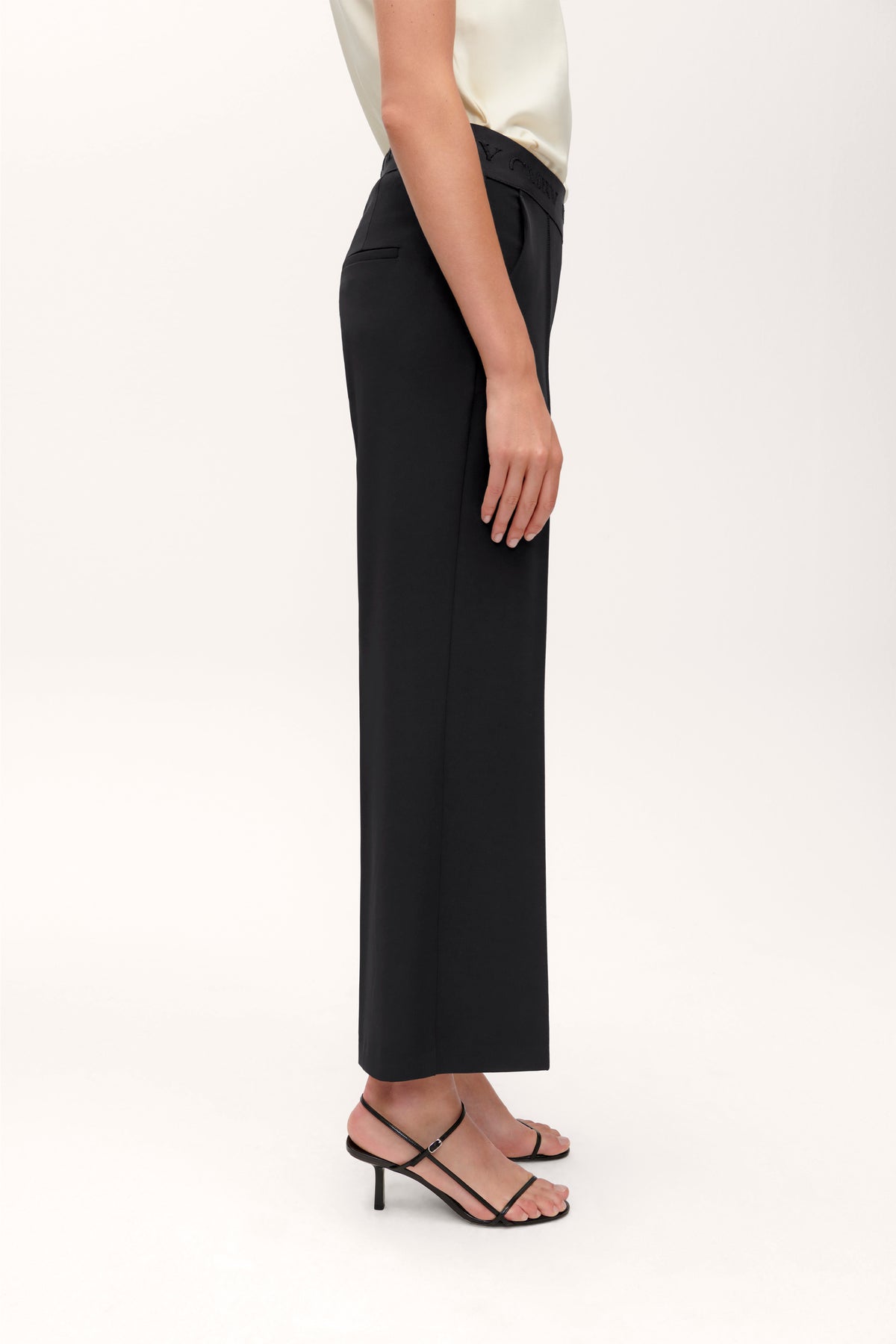 Schwarze Culotte-Hose aus 92% Polyester und 8% Polyurethan, mit weitem Bein und elastischem Bund. Person trägt Heels.