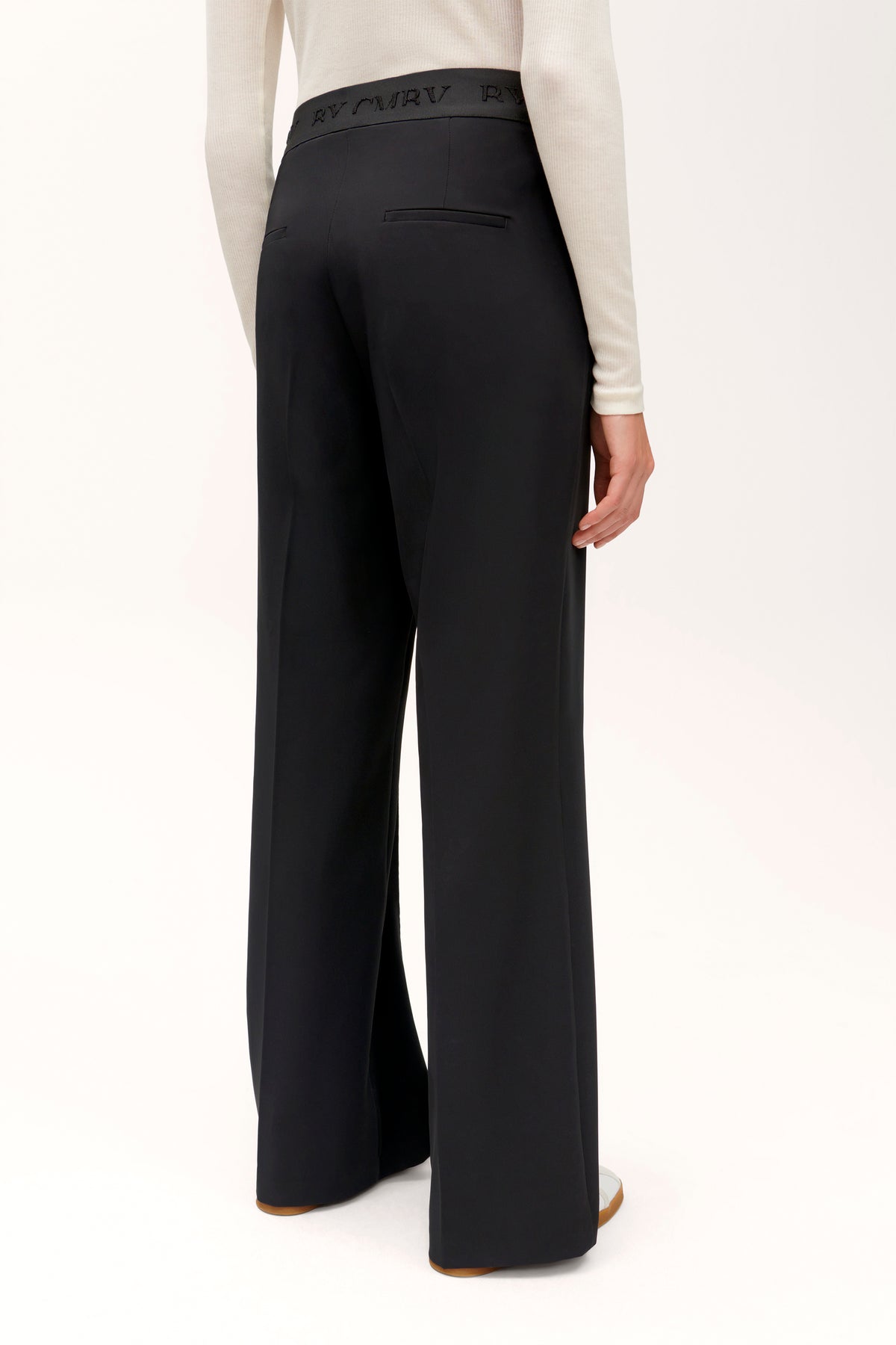 Schwarze, weit geschnittene Hose aus 92 % Polyester und 8 % Polyurethan wird von einer Person in einem neutralen Setting getragen.