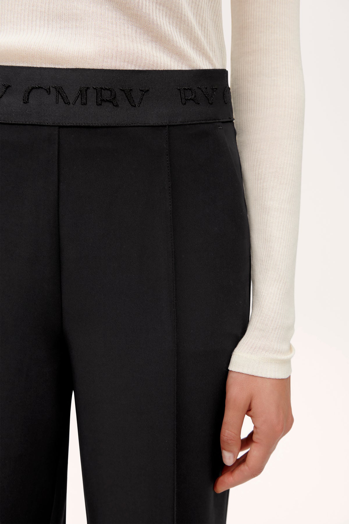 Schwarze weite Hose aus 92% Polyester und 8% Polyurethan, elastischer Bund mit Aufschrift; wird von einer Person getragen.