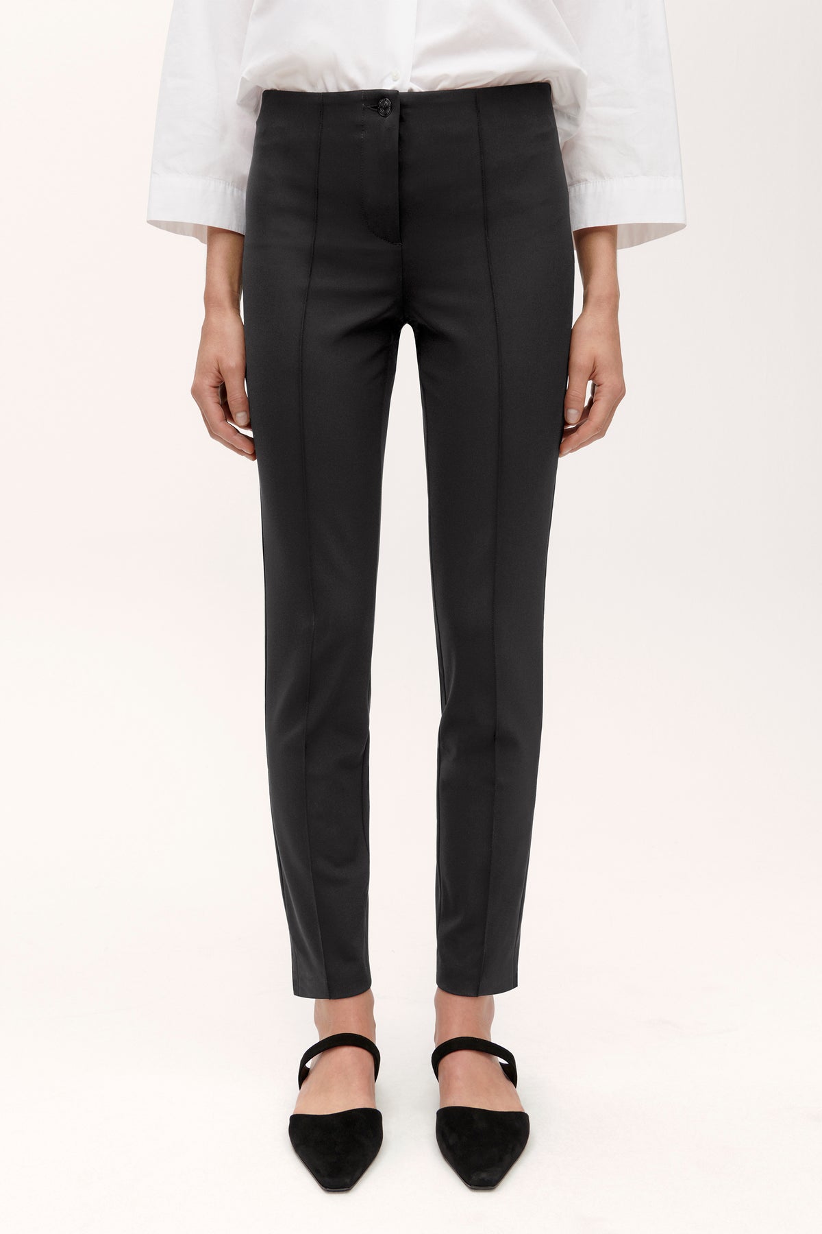 Schwarze Slim-Fit Hose aus 88% Polyamid und 12% Elasthan, mit schmalem Schnitt und Knopfverschluss, getragen in einem Studio. Sie wird mit einem weißen Hemd und schwarzen Schuhen kombiniert.