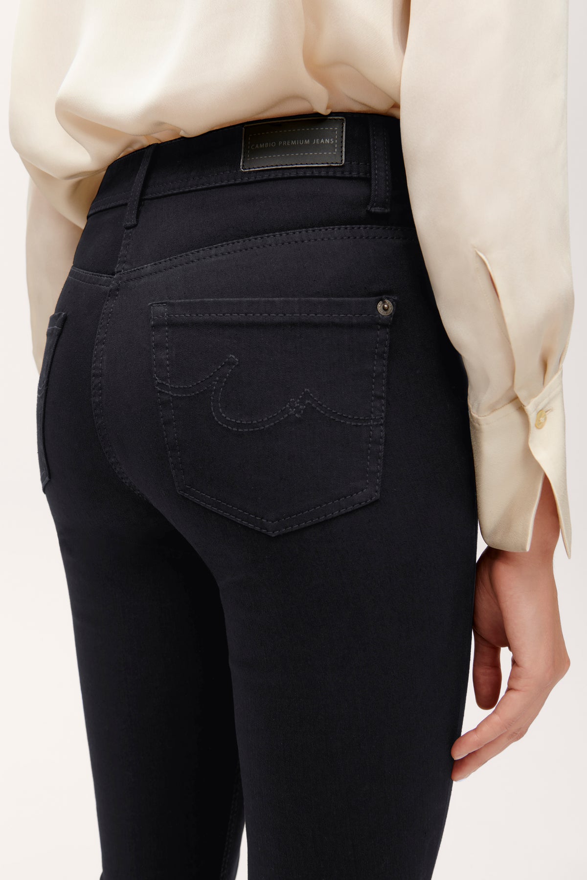 Schwarze Slim-Fit-Jeans aus 77% Baumwolle, 18% PBT, 5% Elasthan, an einer Person getragen. Elegantes Outfit mit beigefarbener Bluse.