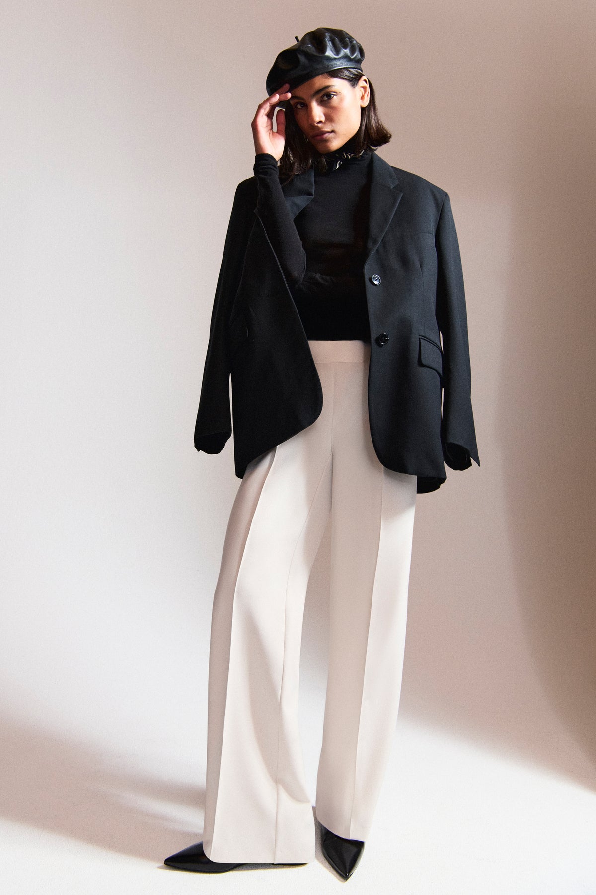 Damen trägt weiße Wide Leg Hose aus Polyester-Bistretch. Dazu ein schwarzes Oberteil und Sakko in einer urbanen Kulisse.