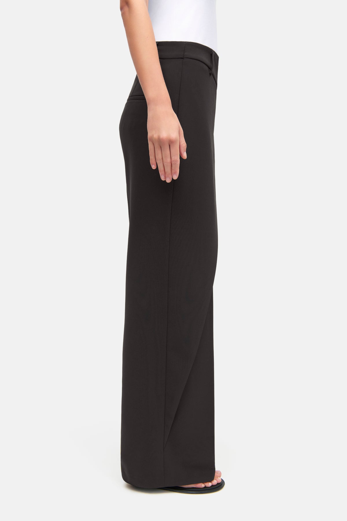 Braune Wide-Leg Hose aus 90% Polyester und 10% Polyurethan. Person steht seitlich in lässigem, alltäglichem Umfeld.