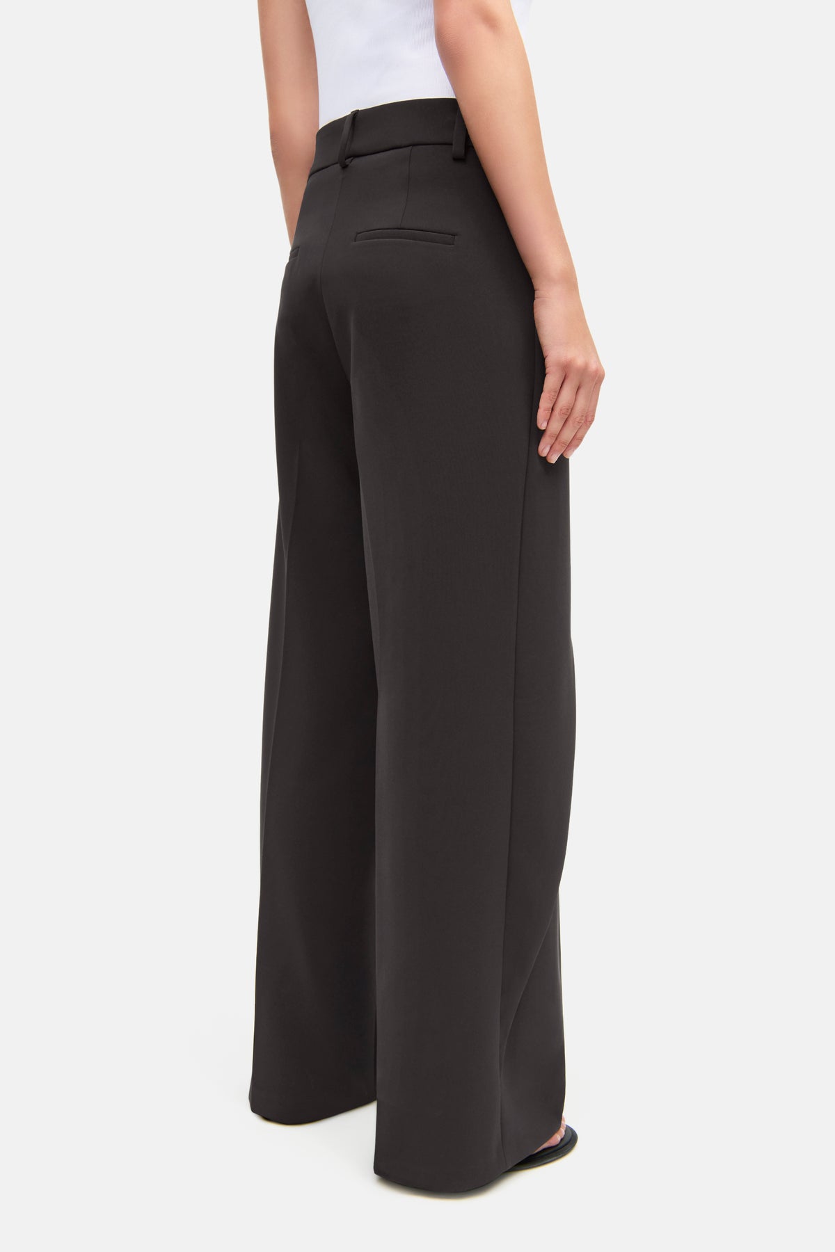 Braune, weite Hose aus 90% Polyester, 10% Polyurethan. Asymmetrischer Bund, eleganter Stil. Person trägt sie in einem Alltagssetting.