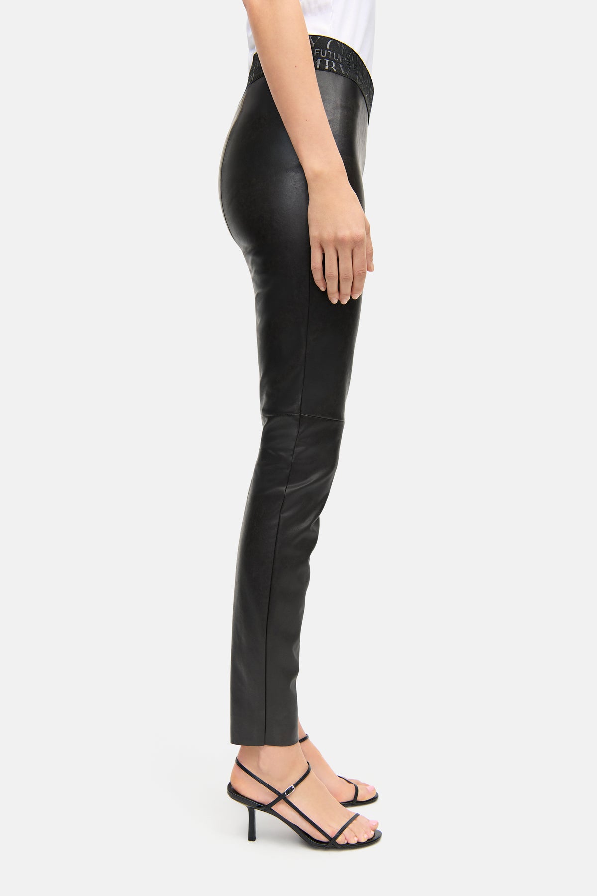 Schwarze Skinny-Fit-Hose aus veganem Nappa mit elastischem Bund. Bein einer Person in Profilansicht, trägt Sandaletten.