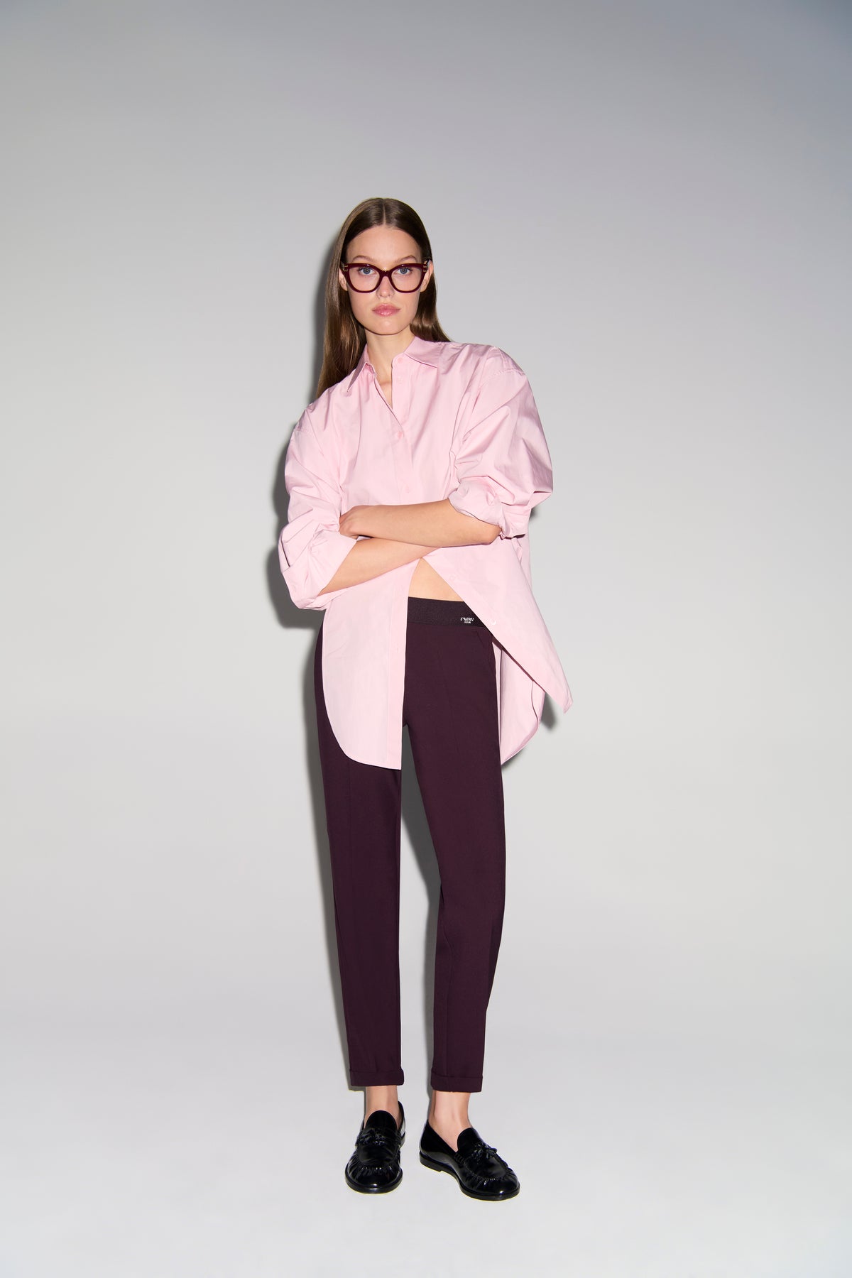 Bordeauxfarbene Karottenhose aus 63 % Polyester, 27 % Viskose, 7 % Baumwolle, 3 % Elasthan, getragen in einem Studio-Setting.