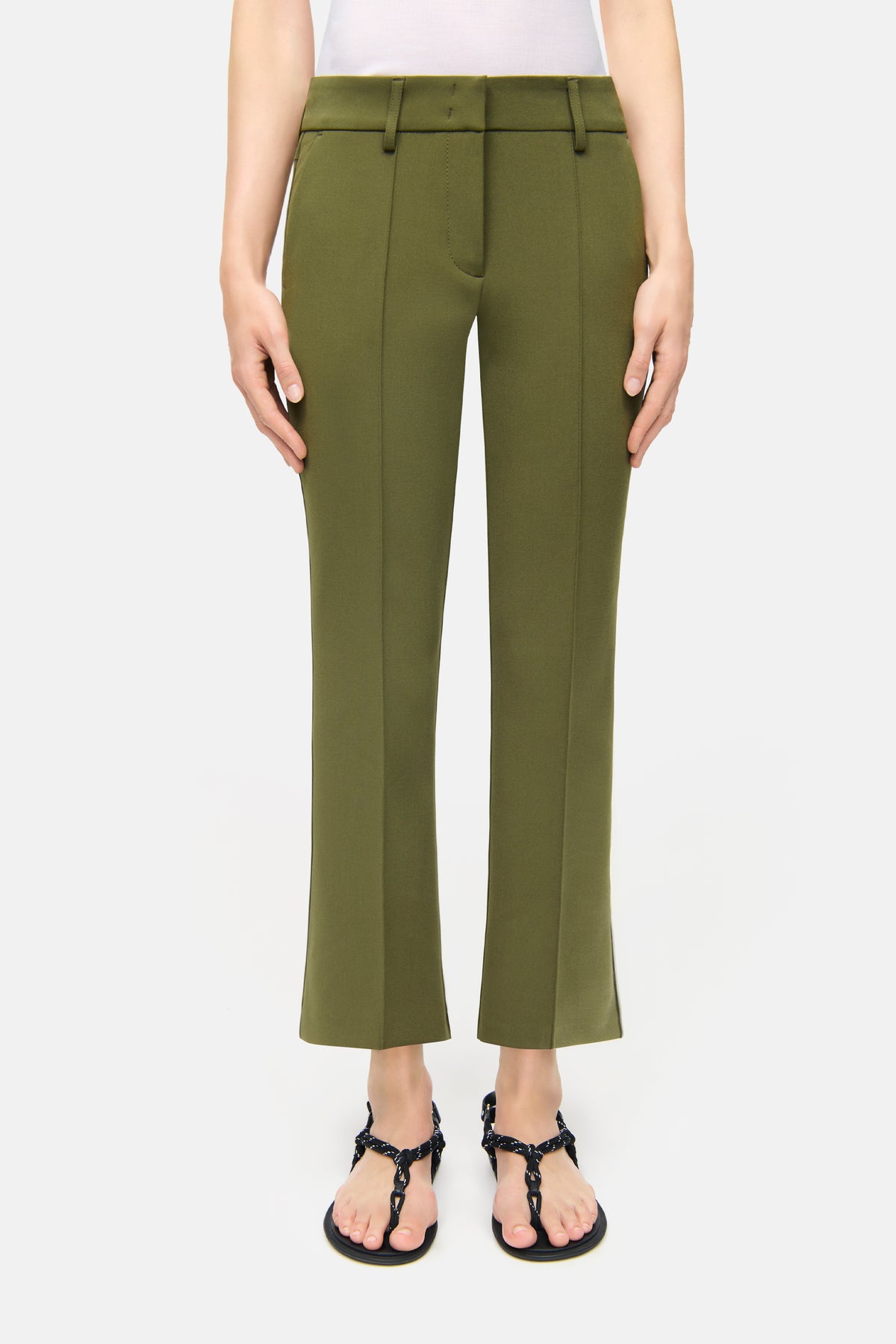 Grüne Flared-Hose aus 7% Baumwolle, 63% Polyester, 3% Elasthan, 27% Viskose, getragen in einem minimalistischen, neutralen Setting.