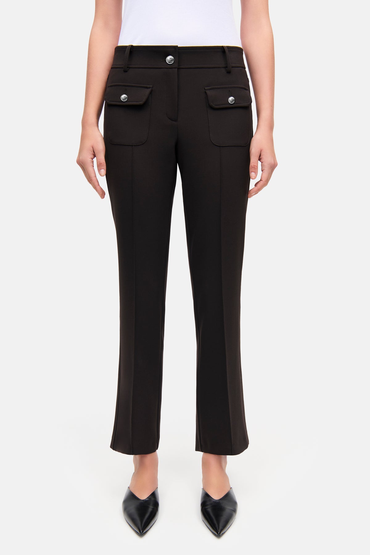 Dunkelbraune Flared-Hose mit silbernen Knöpfen und aufgesetzten Taschen, aus Baumwolle, Polyester, Elasthan und Viskose. Die Hose wird in einem Studio von einer Person getragen.