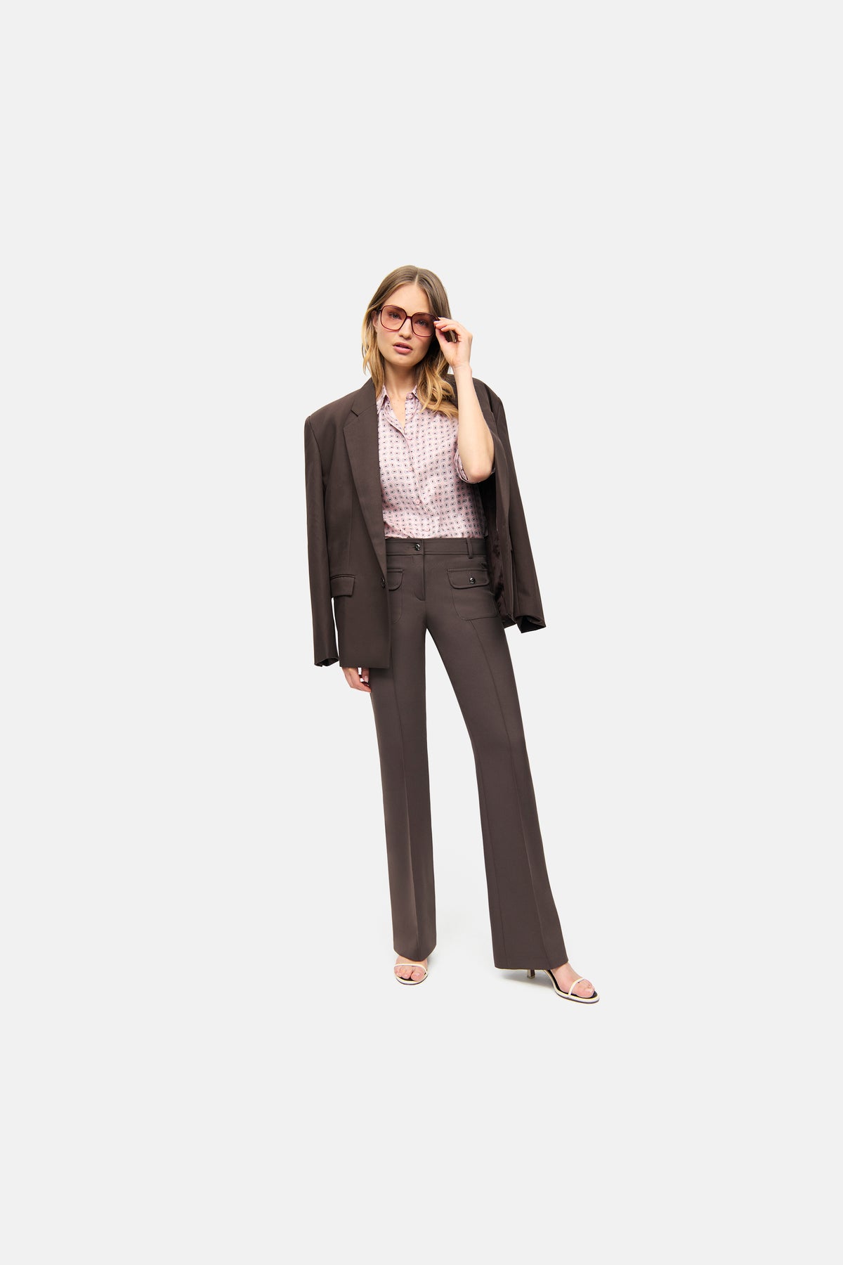 Braune Schlaghose aus Bi-Stretch-Material mit silberfarbenen Knöpfen und aufgenähten Fronttaschen, getragen in einem urbanen Setting.