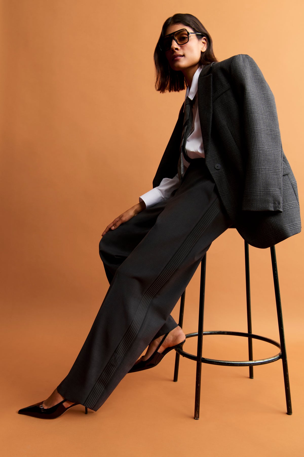 Dunkelgraue Glam Slouch Track Hose aus Woll-Melange, Karotten-Form mit Bügelfalten, getragen von Person auf einem Hocker sitzend.