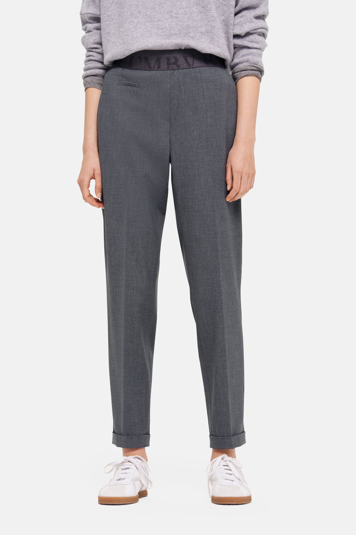 Graue Karottenhose aus 67% Polyester, 29% Viskose, 4% Elasthan, getragen mit Turnschuhen in einem lässigen Stil.