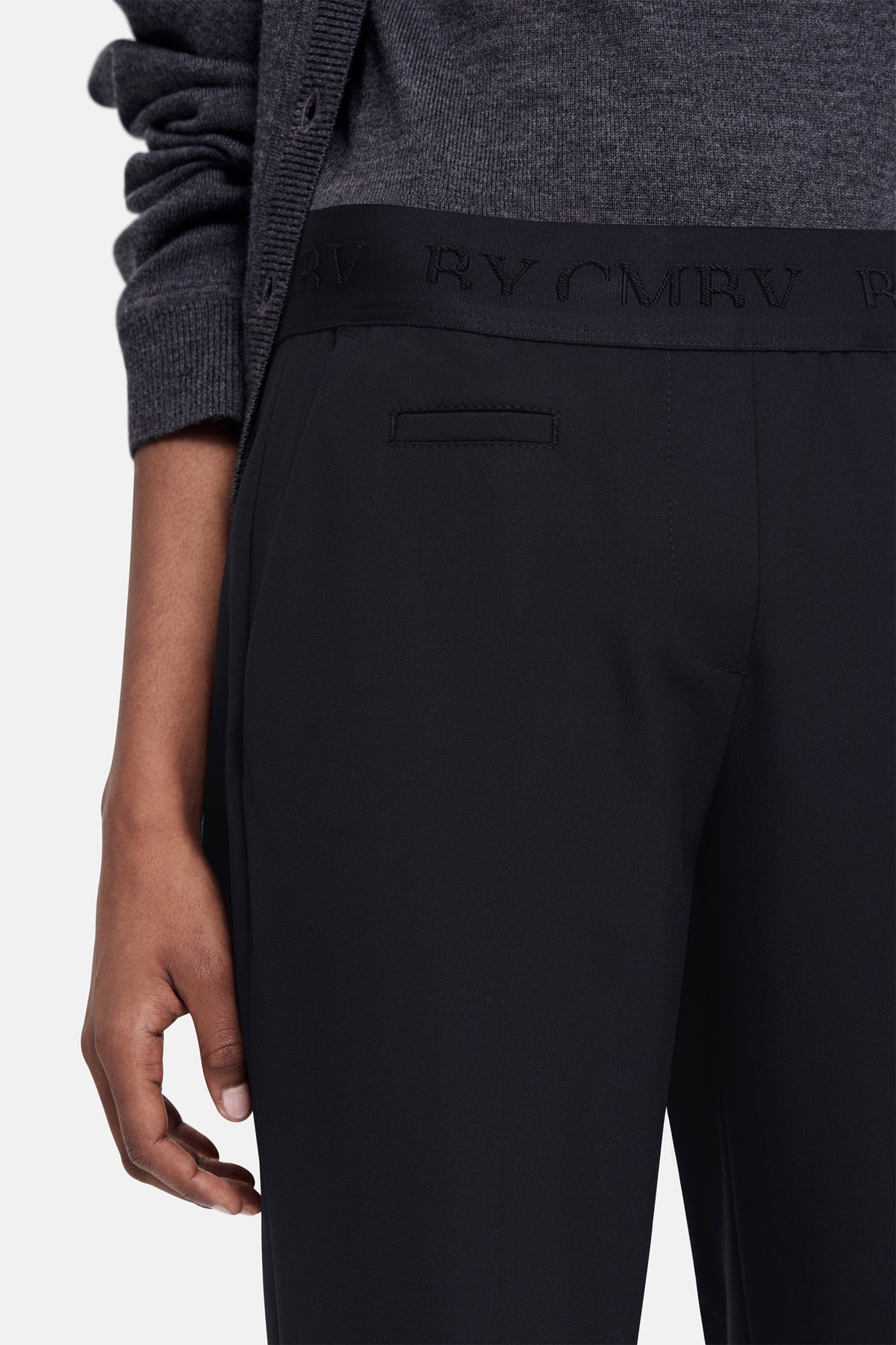 Schwarze Carrot-Fit Hose aus 67% Polyester, 29% Viskose, 4% Elasthan. Person in lässigem Setting mit grauem Oberteil.