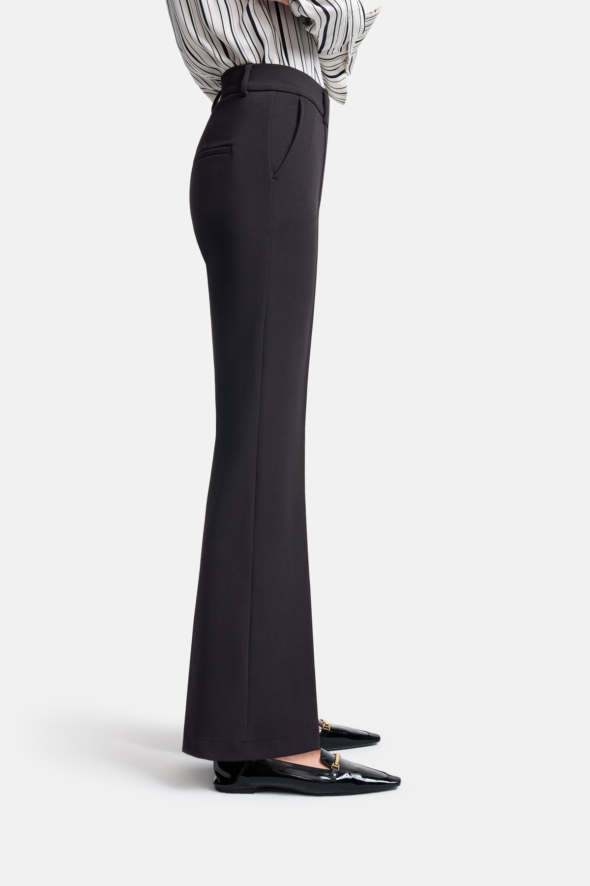 Schwarze Flared-Hose in voller Länge aus Diagonal Structure Techno Stretch. Material: 95 % Polyamid, 5 % Elasthan. Getragen in einem Indoor-Setting, kombiniert mit schwarzen Schuhen.