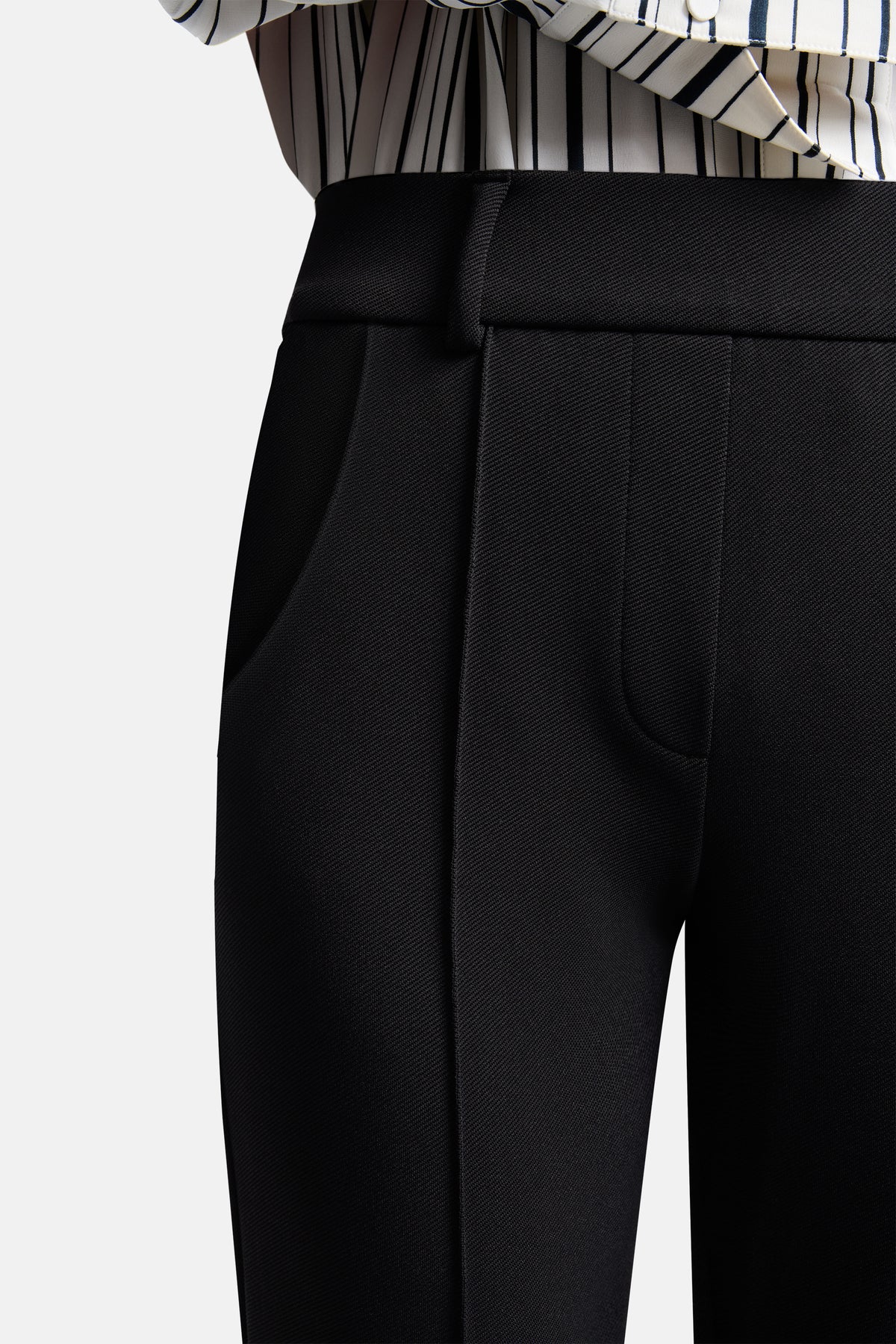 Schwarze Flared-Fit Hose aus 95% Polyamid und 5% Elasthan. Die Hose hat eine diagonale Struktur. Person trägt Streifenbluse.