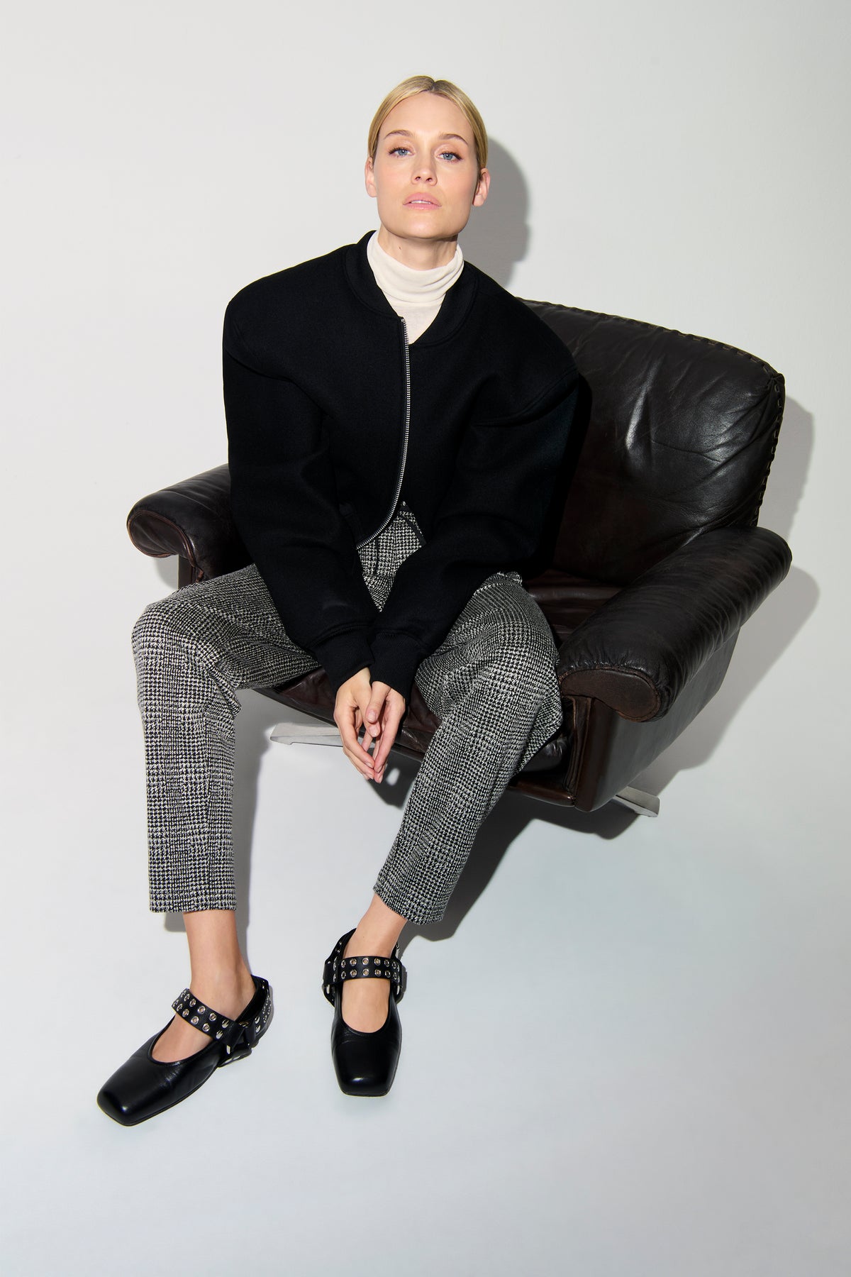 Frau sitzt auf Ledersessel, trägt karierte O-Shape Hose in Schwarz-Weiß aus Viskosemischung, kombiniert mit schwarzem Oberteil.
