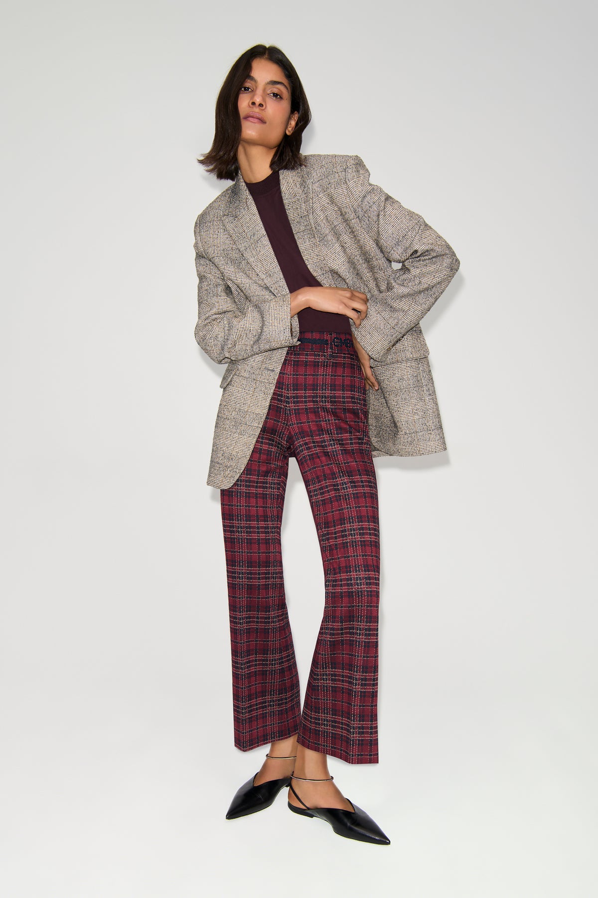Bordeauxfarbene, karierte Hose im Flared-Fit aus 57% Viskose, 39% Polyamid, 4% Elasthan, getragen in einem urbanen Kontext.