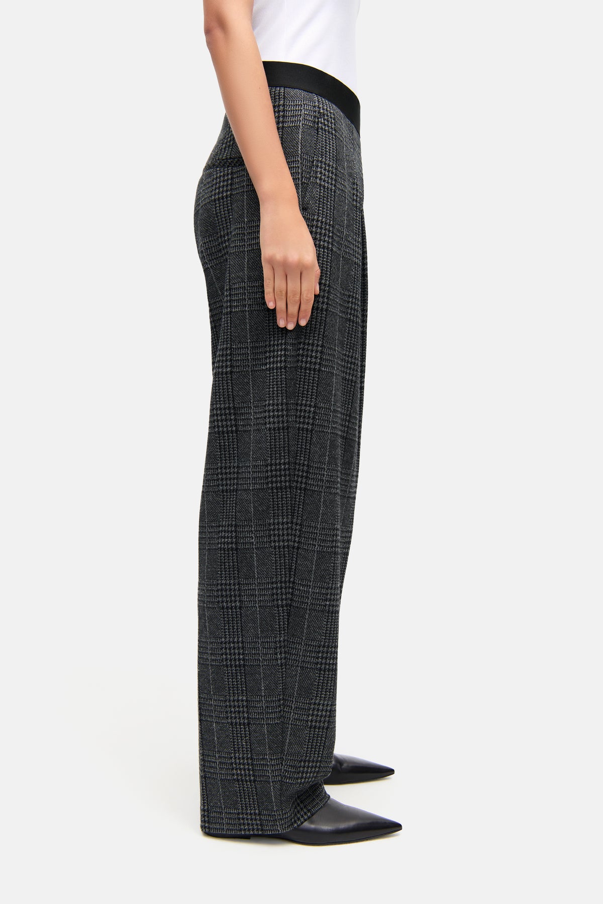 Graue O-Shape Hose aus Brushed Glencheck Jersey, getragen von einer Person, kombiniert mit einem weißen Oberteil und schwarzen Schuhen.
