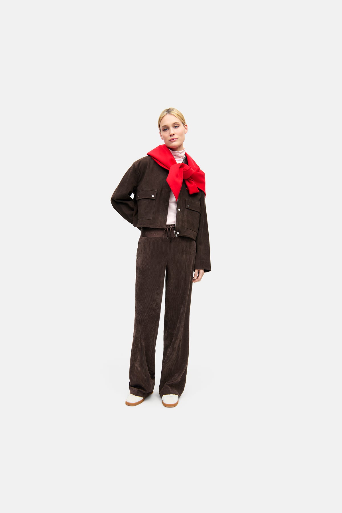 Dunkelbraune Wide Leg Hose aus 90% Polyester, 8% Polyamid, 2% Elasthan. Getragen im urbanen Setting mit roter Strickjacke.
