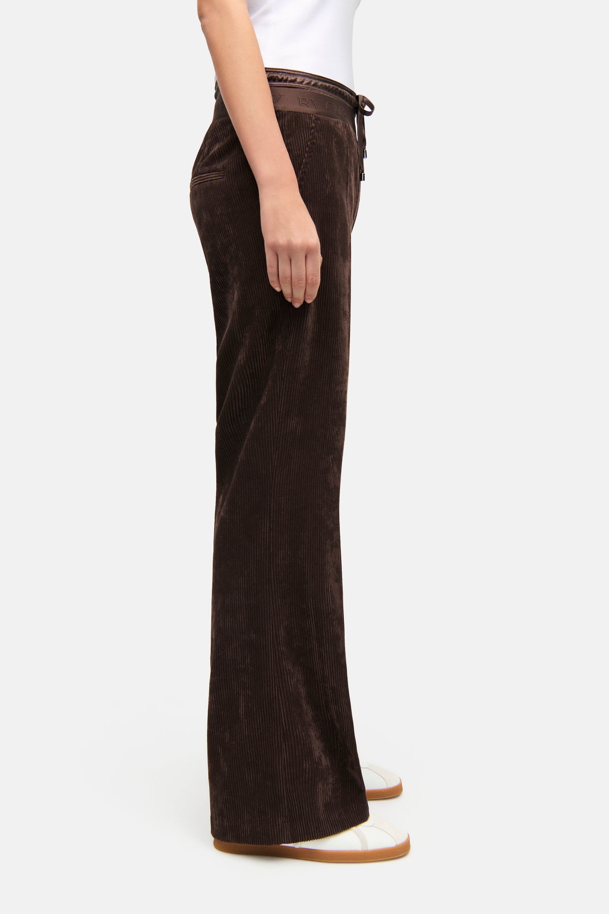 Dunkelbraune Hose mit weitem Bein aus Breit-Cord, Doppelbund mit Schnürung, Material: 90% Polyester, 8% Polyamid, 2% Elasthan. Person steht seitlich mit weißen Schuhen.