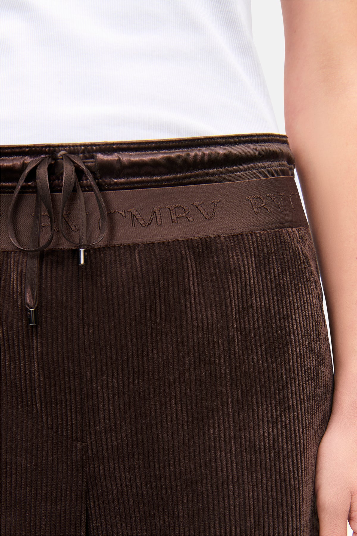 Dunkelbraune Breitcord-Hose mit weitem Bein und elastischem, dekorativem Doppelbund. Material: 90% Polyester, 8% Polyamid, 2% Elasthan. Die Hose wird in einer entspannten Umgebung getragen.