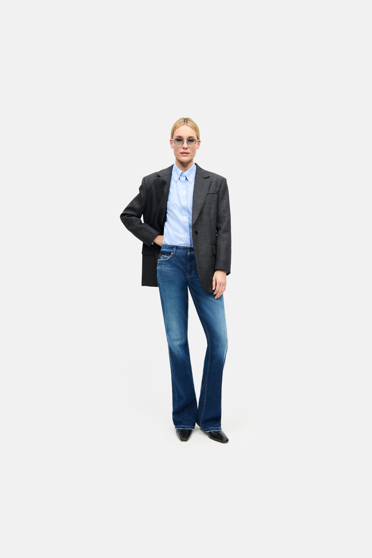 Person in einem formellen Outfit mit blauer, ausgestellter Jeans aus Baumwolle und Elasthan, in einem urbanen Setting.