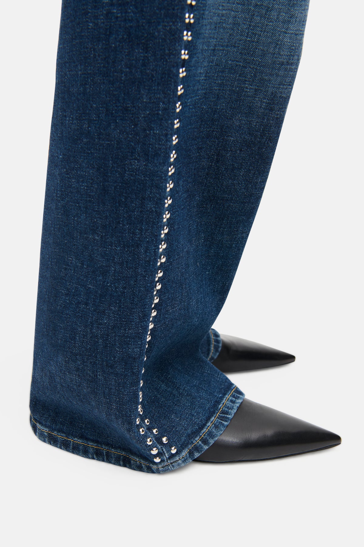 Blaue Jeans im Wide Leg-Stil mit dekorativen Nieten an den Seiten. Material: 98% Baumwolle, 2% Elasthan. Getragen mit schwarzen spitzen Schuhen.