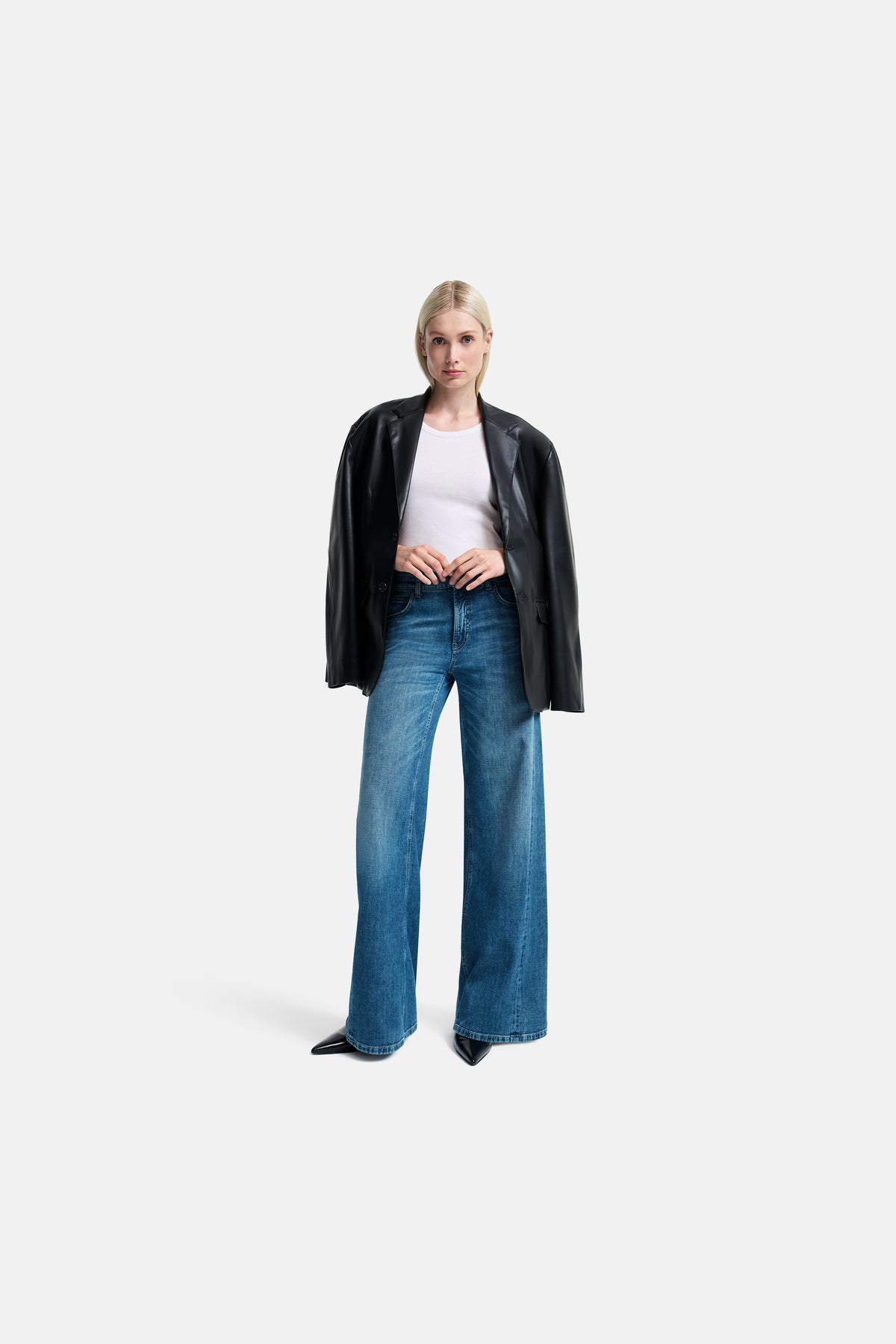 Weite Palazzo-Jeans in heller blauer Waschung, aus 92% Baumwolle, 6% Elastomultiester T400, 2% Elasthan. Die Hose wird von einer Person in einem minimalistischen Studioambiente getragen, kombiniert mit einer schwarzen Lederjacke und einem weißen Oberteil.