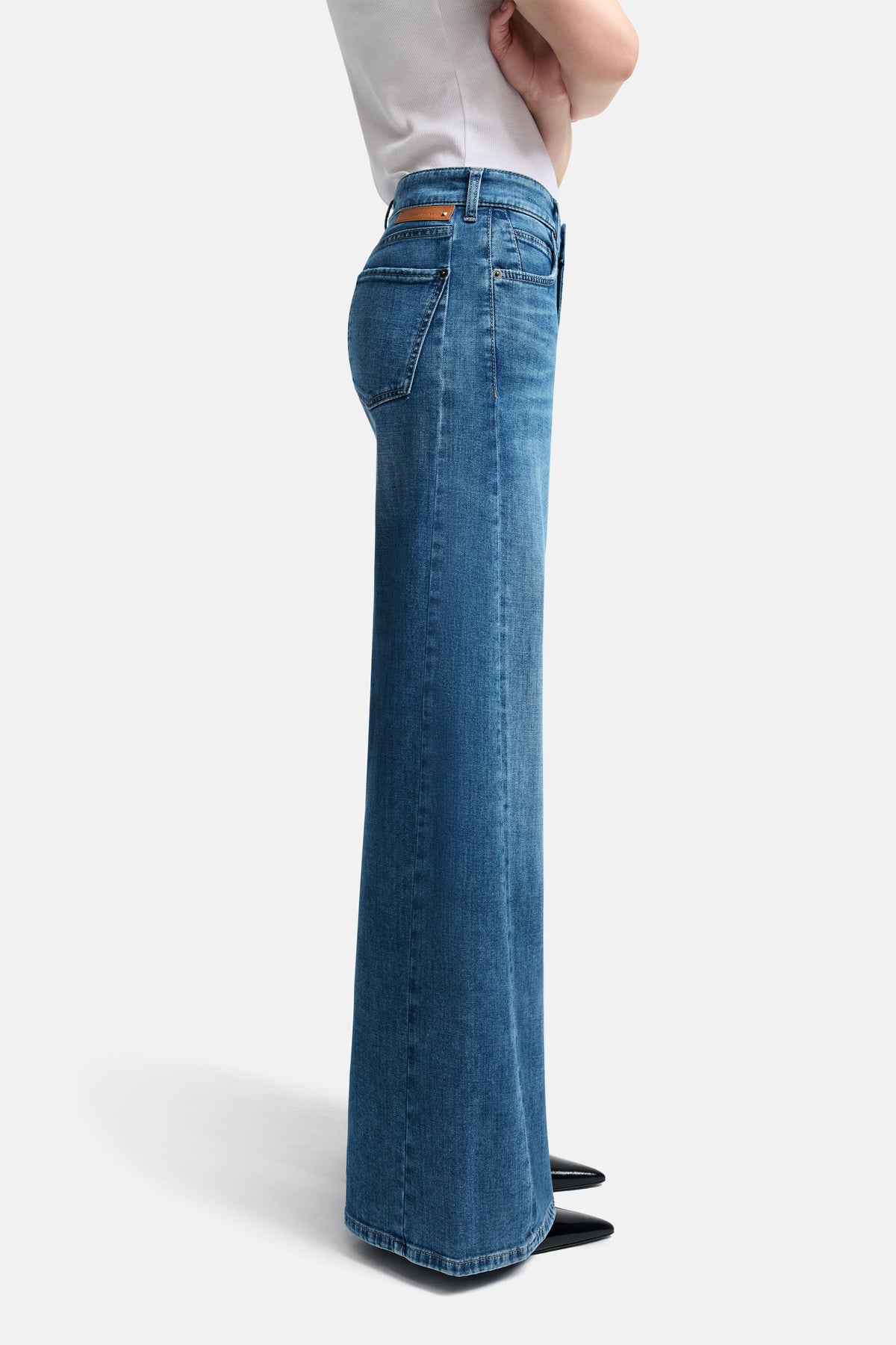 Blaue Palazzo-Jeans aus Denim mit weitem Bein und kontrastreichem Einsatz am Bein. Material: 92% Baumwolle, 6% Elastomultiester T400, 2% Elasthan. Person steht im Profil mit überkreuzten Armen.